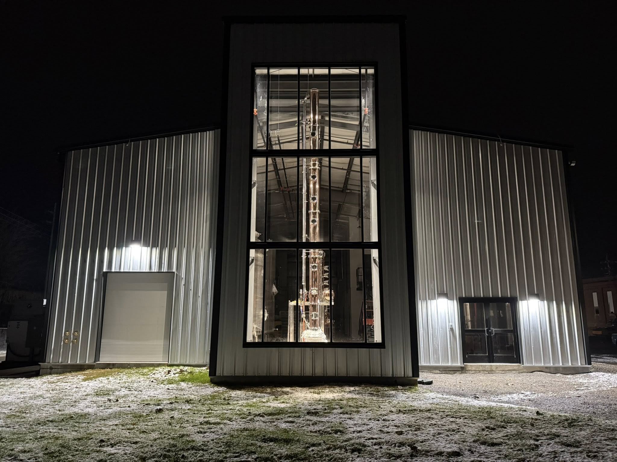 Nighttime view of a modern building with metallic siding and large glass windows revealing a tall, intricate scientific instrument inside.