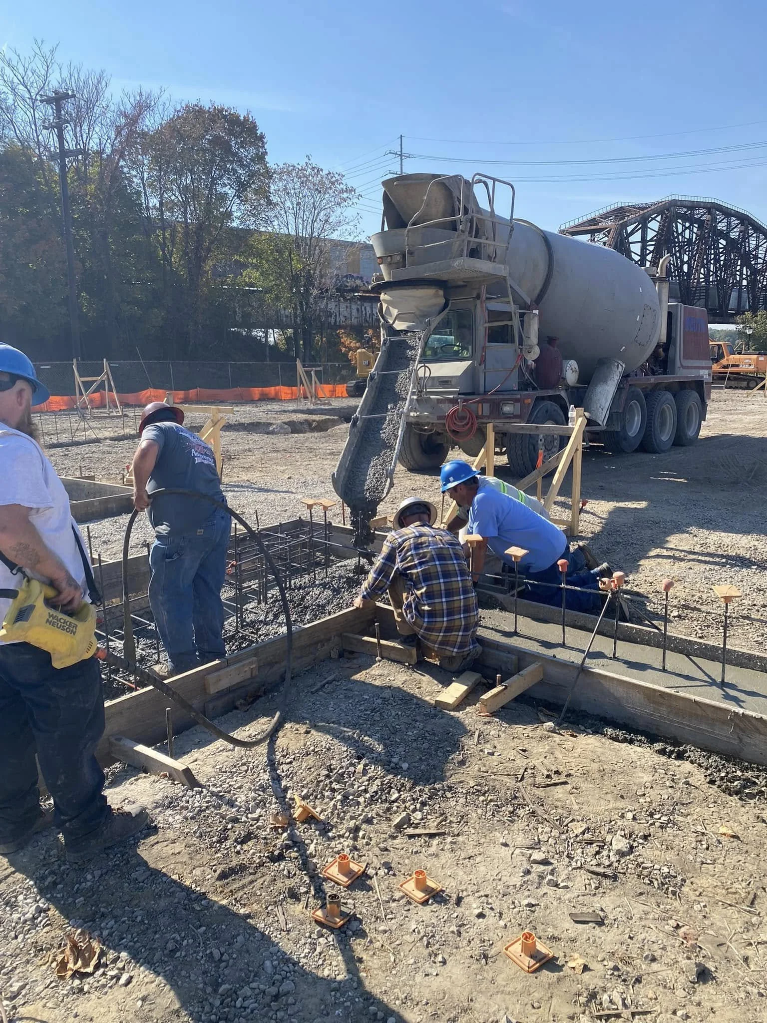 Construction workers pouring concrete for a foundation slab at a construction site with a concrete mixer truck in the background.