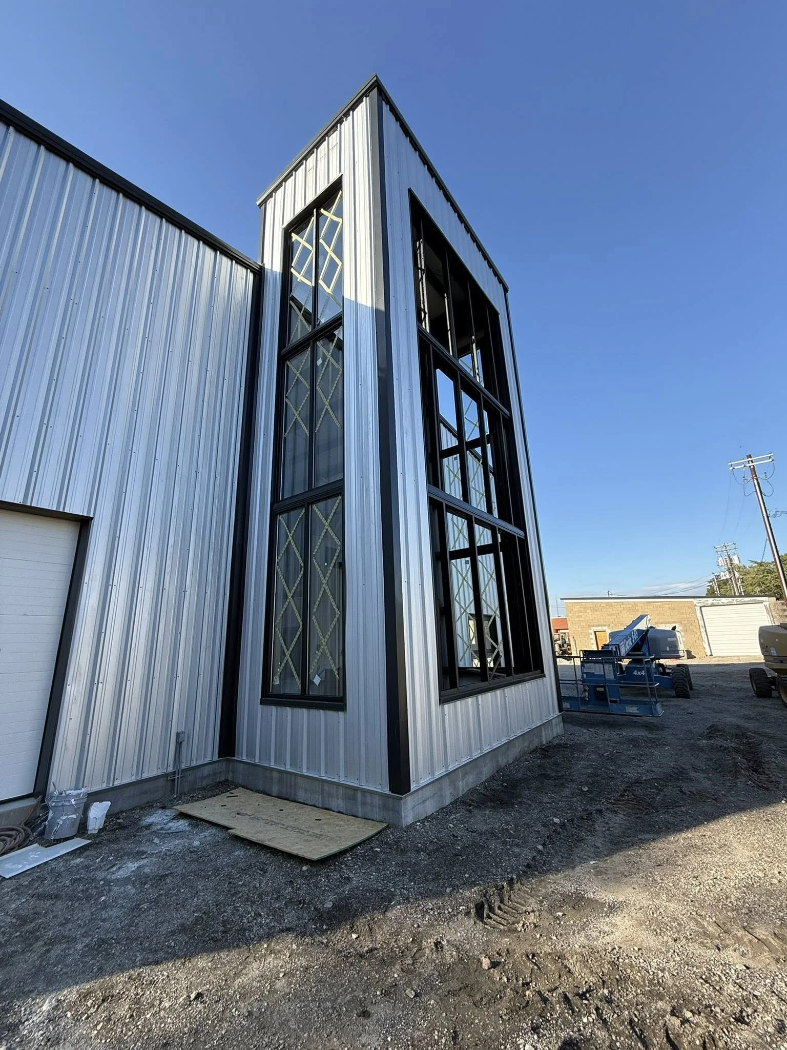 Under construction modern building with metal siding and large glass windows, blue sky in the background.