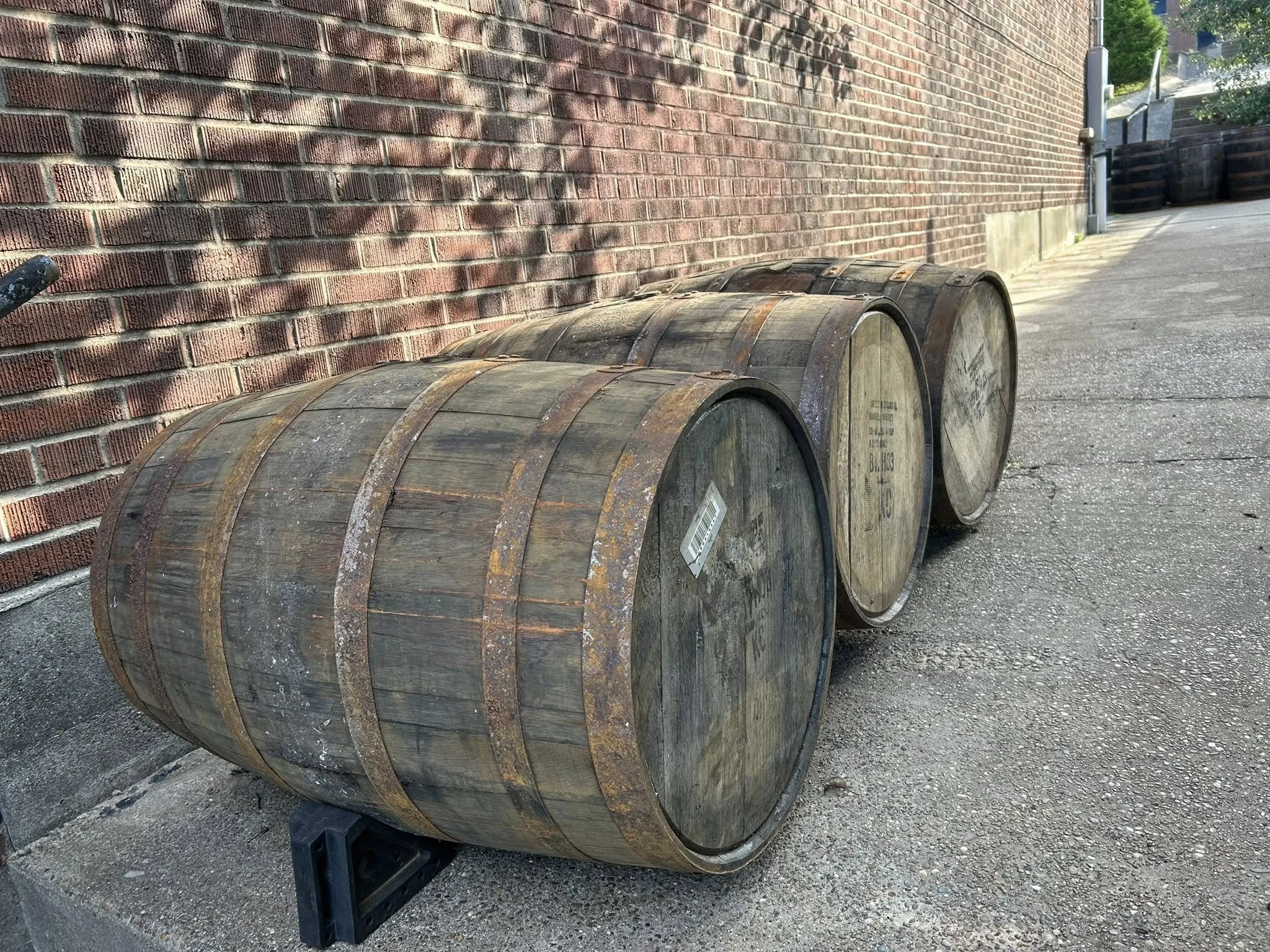 Three wooden barrels lying on their sides outdoors on a concrete surface near a brick wall.