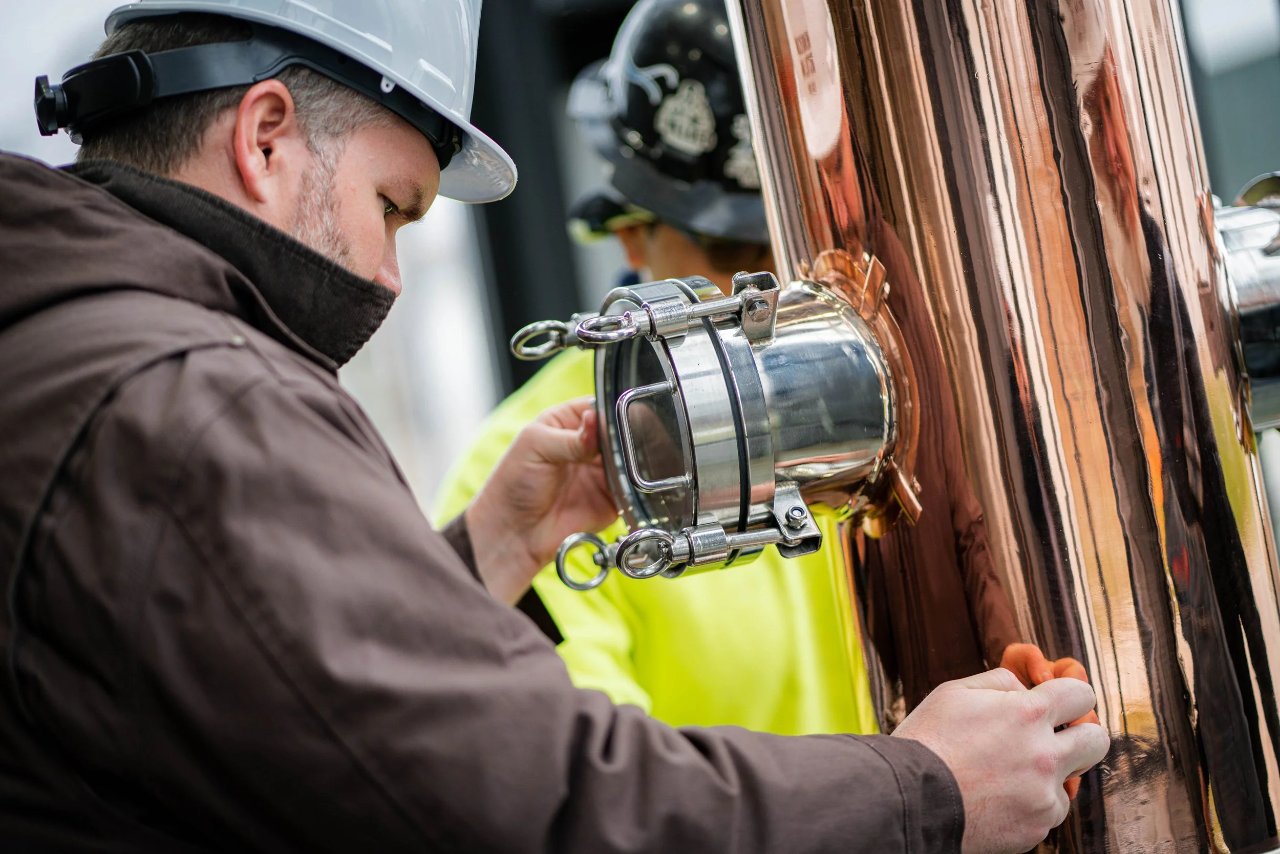 Engineer inspecting a shiny, copper-colored metal pipe on an industrial machinery.