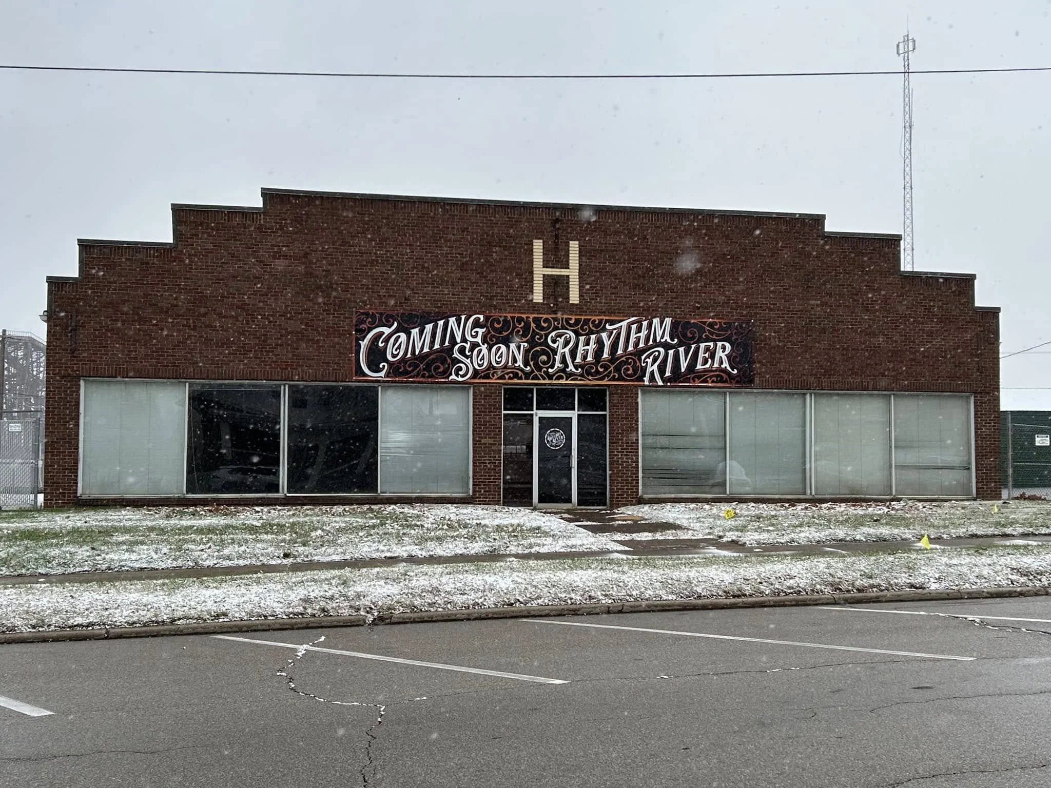 Red brick building with a sign that says 'Coming Soon Rhythm River,' and a large letter H on the top.