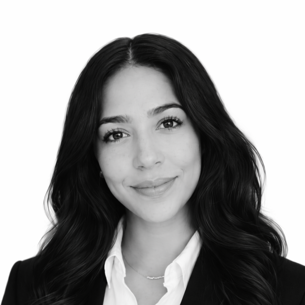 Black and white headshot of a young woman with long, wavy hair, smiling, wearing a white shirt and dark blazer.