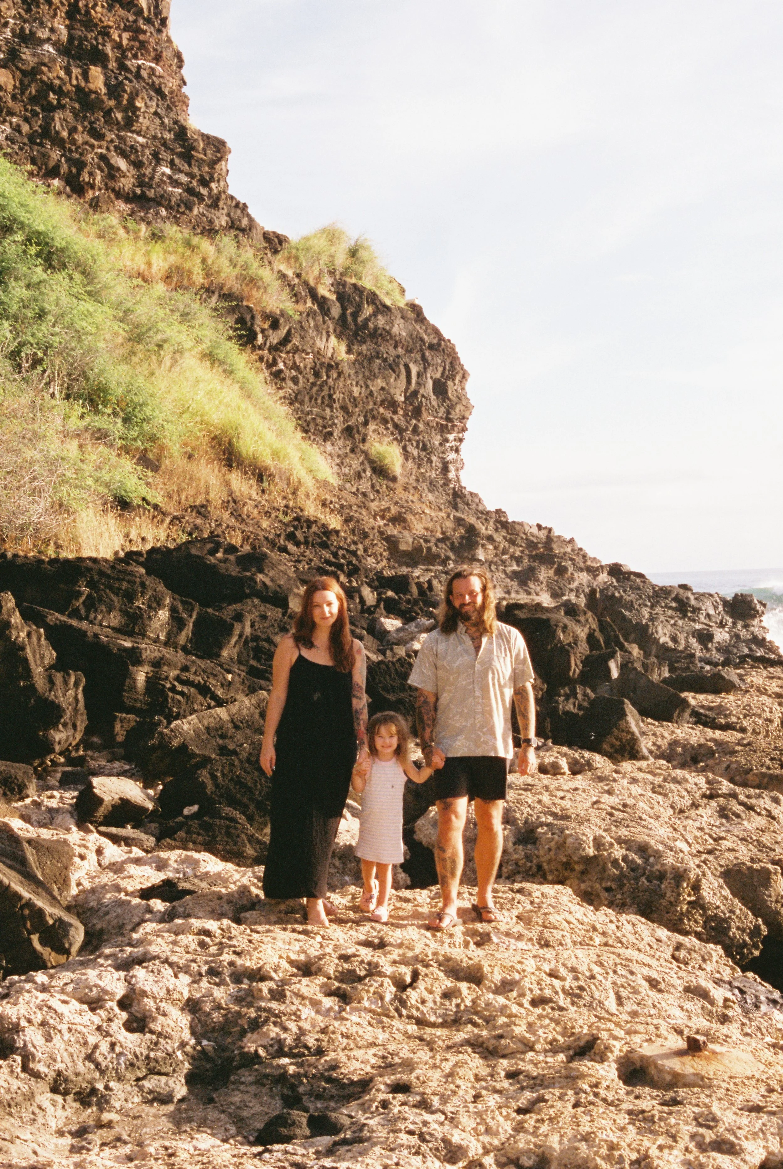 A family of four walking on a rocky beach with cliffs and greenery in the background during daylight.
