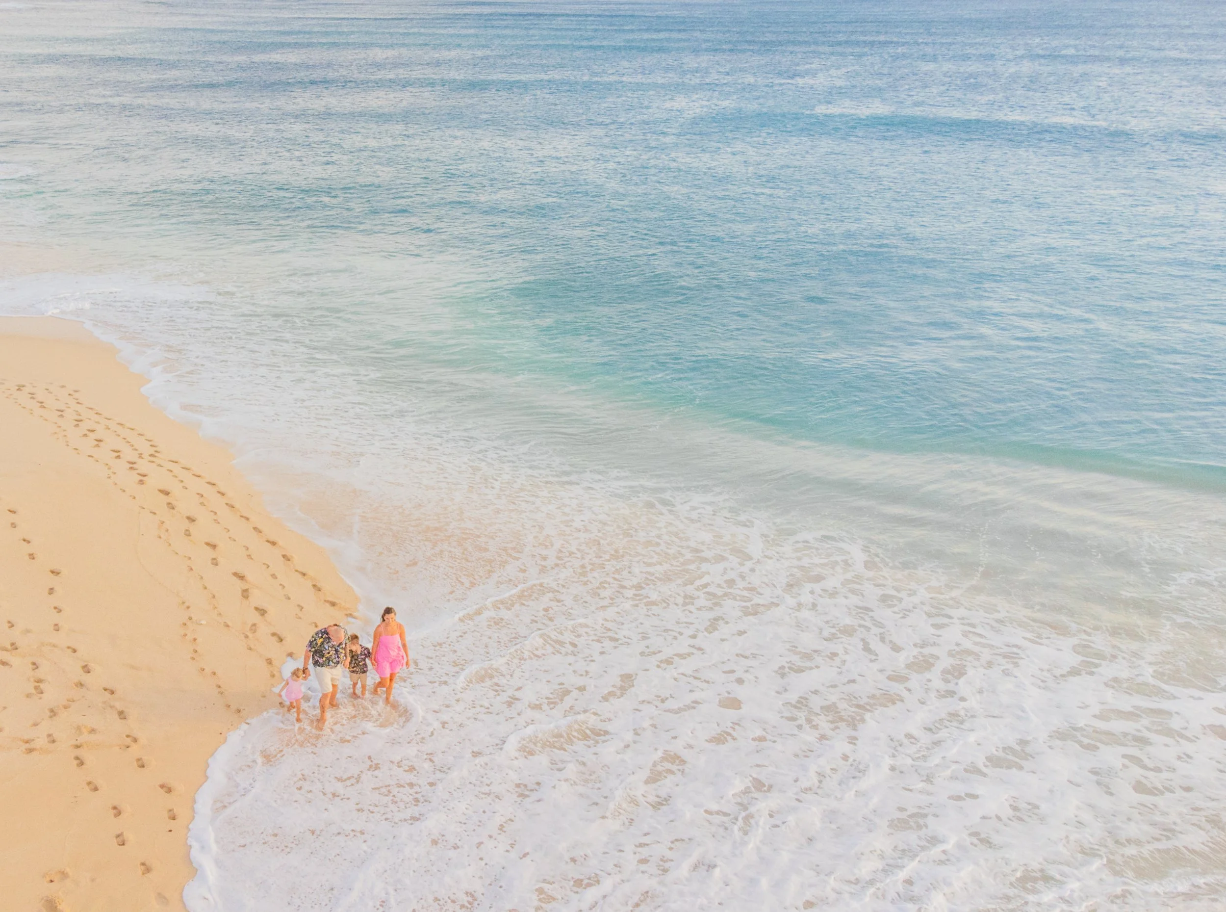 A family of four walking along a sandy beach near the shoreline where the ocean waves meet the sand.