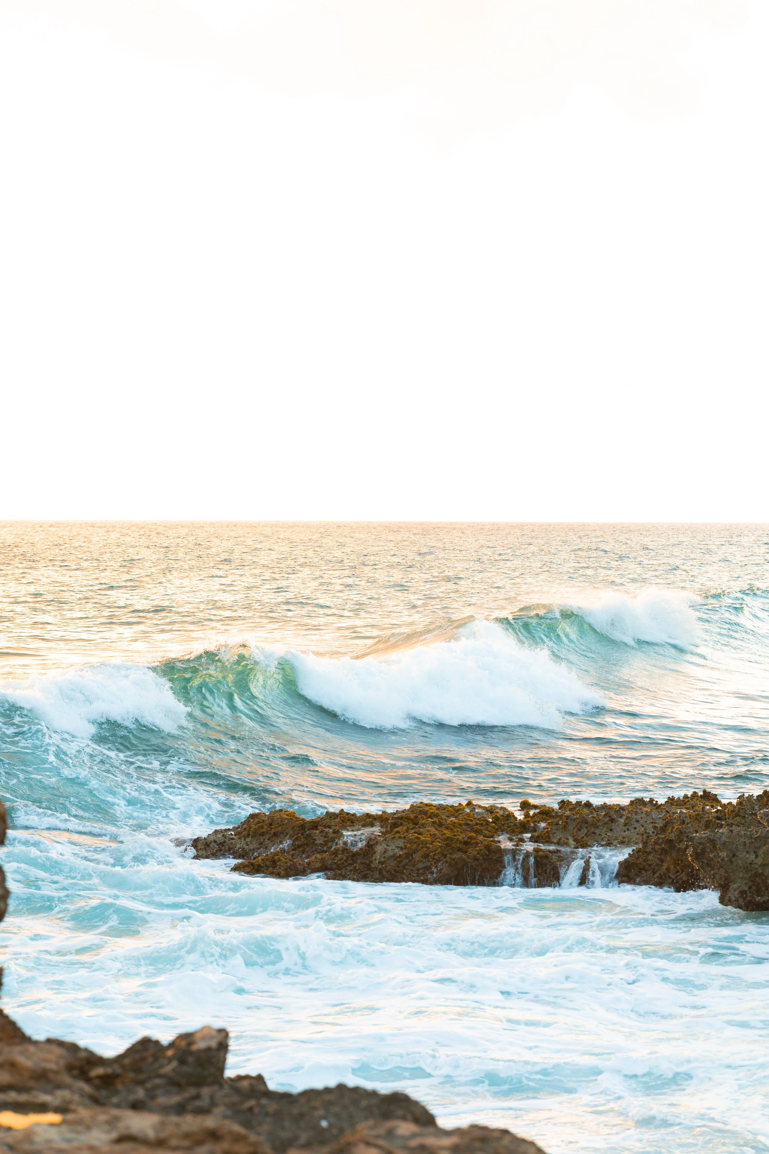 Ocean waves crashing against rocky shoreline during sunset.