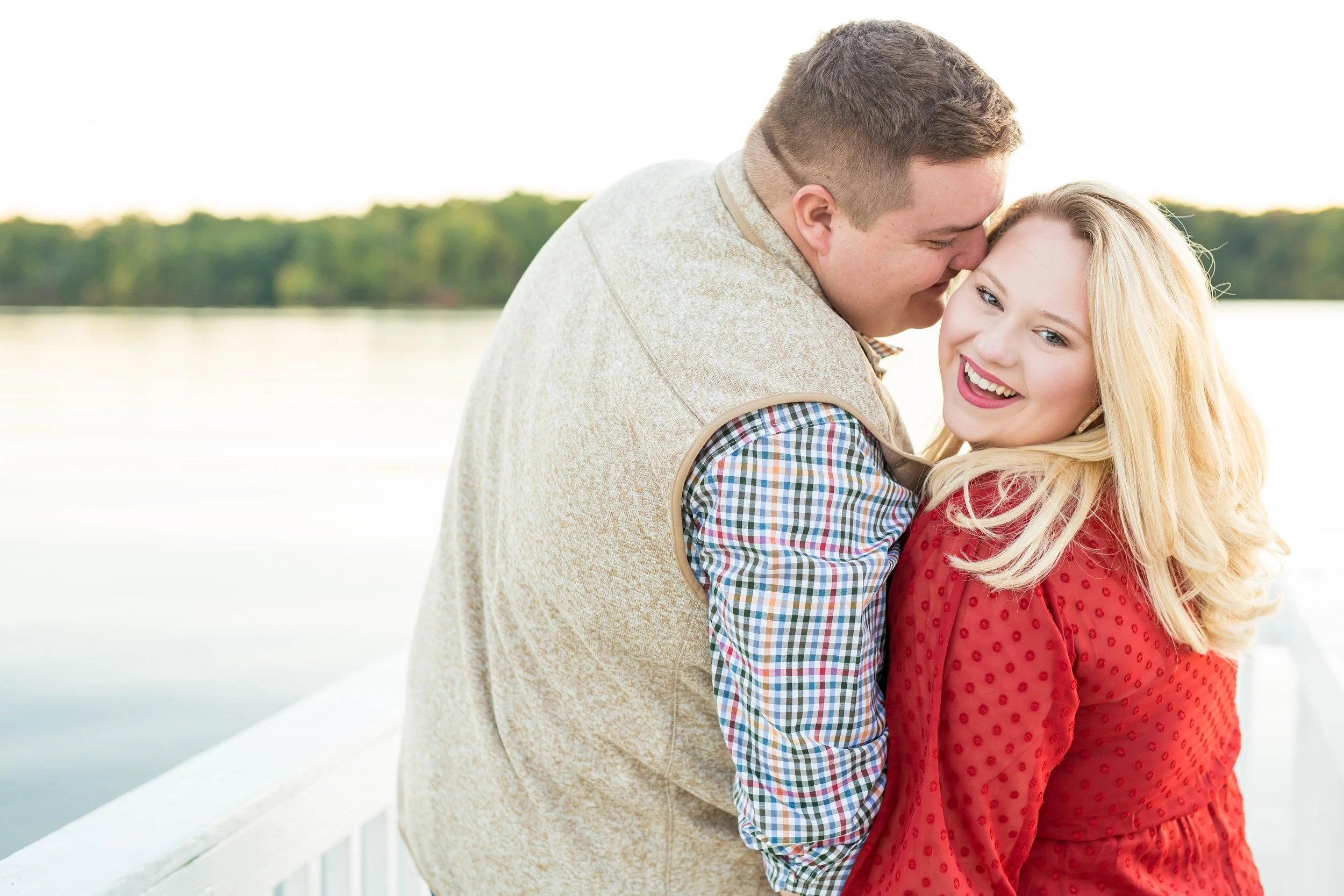 A happy couple embracing on a boat by a lake with trees in the background during sunset.