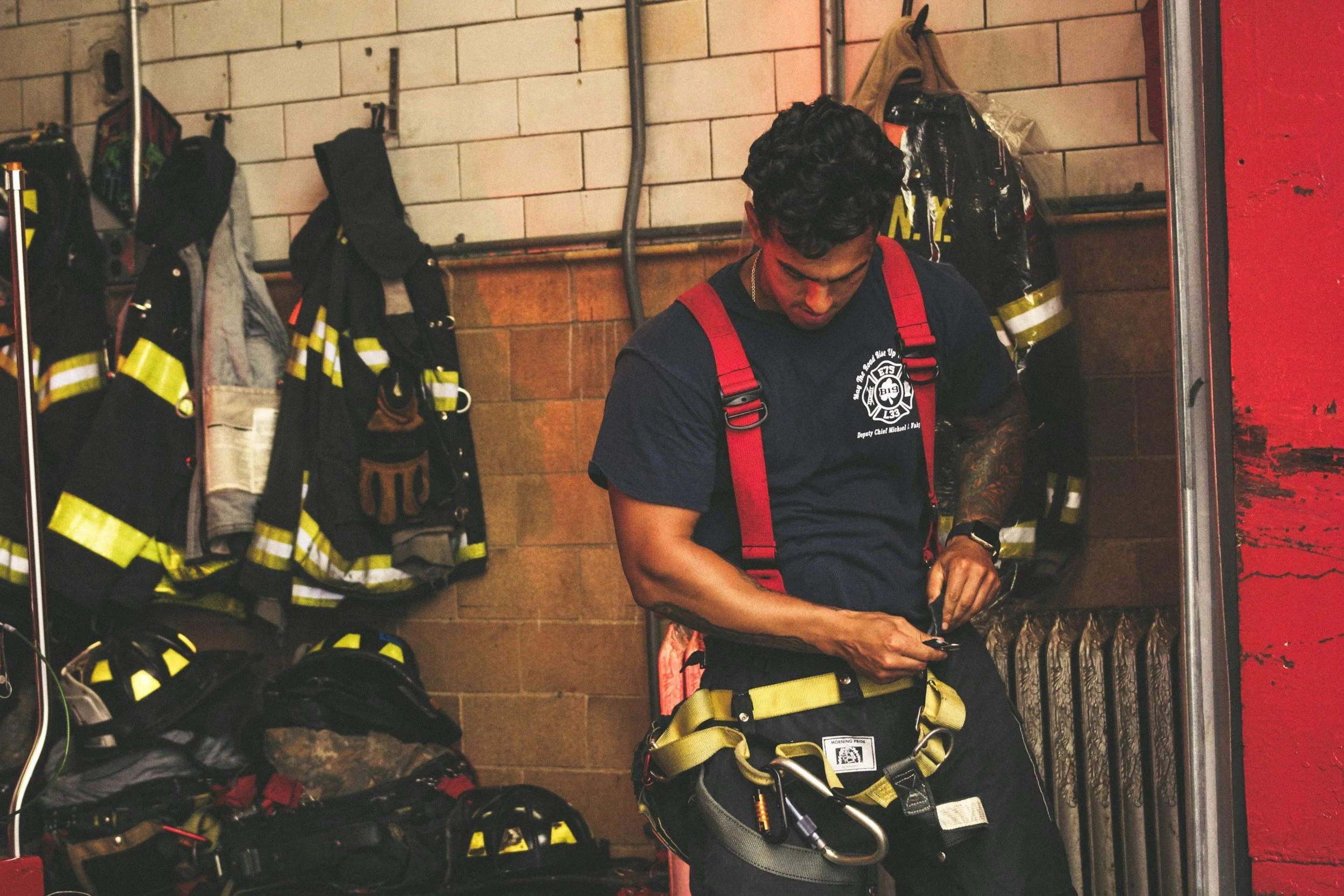 Firefighter in uniform getting ready, surrounded by hanging gear and equipment in a fire station.
