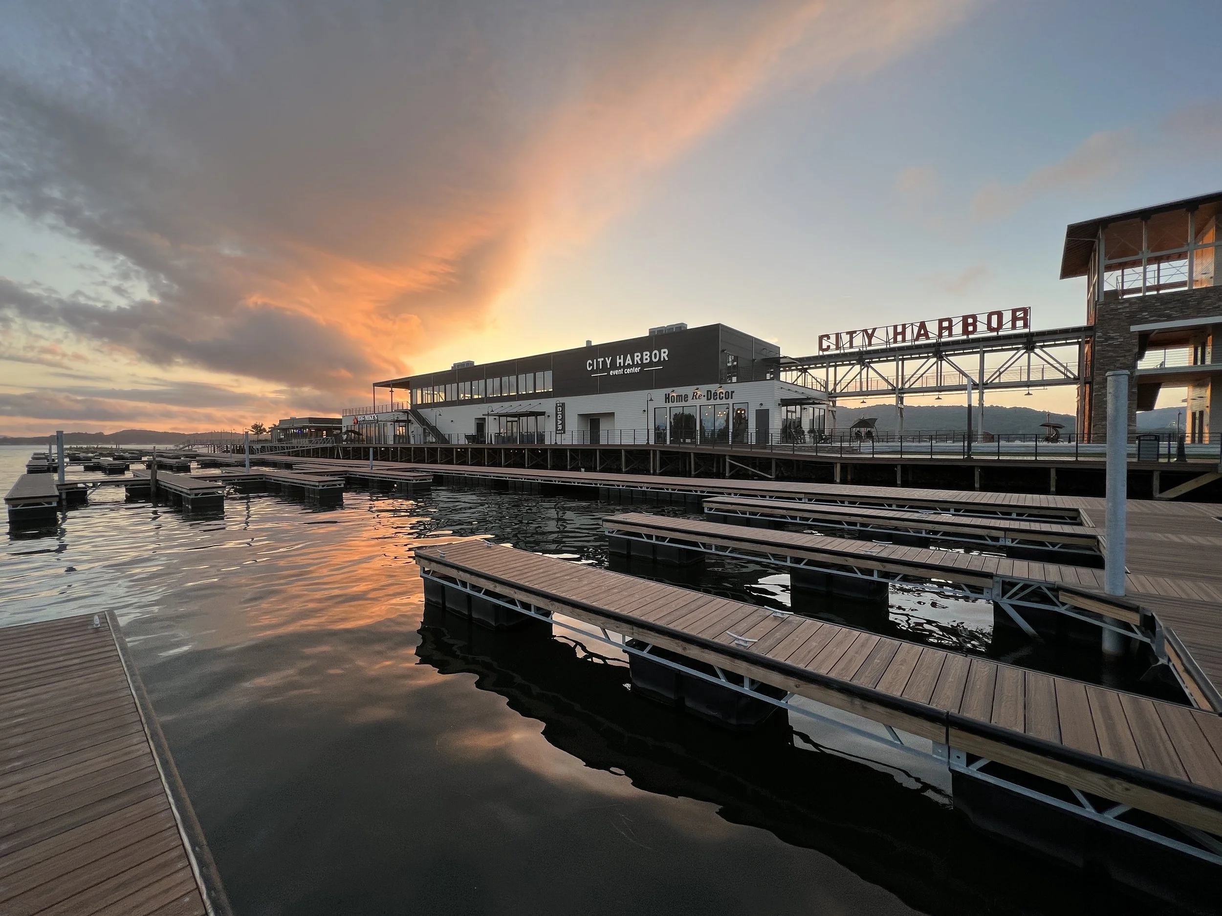 A marina at Lake Guntersville with empty docks at sunset, featuring the City Harbor event center and waterfront buildings