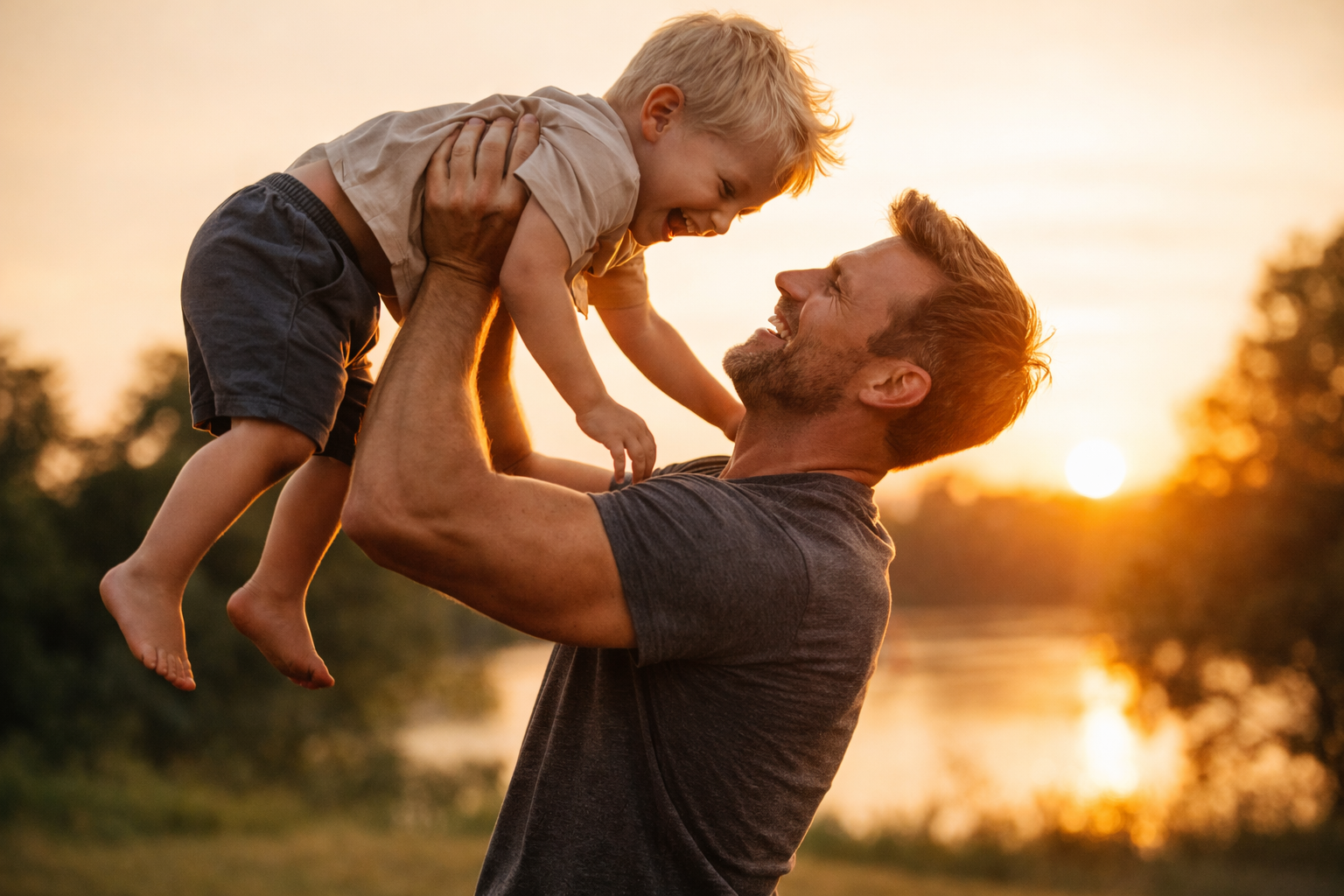 A man lifting a young boy into the air during sunset outdoors, both smiling and enjoying a joyful moment.