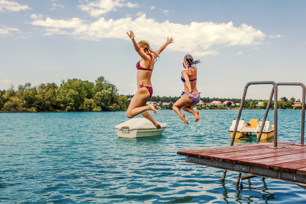 Two young women jumping into Lake Guntersville from a dock on a sunny day.