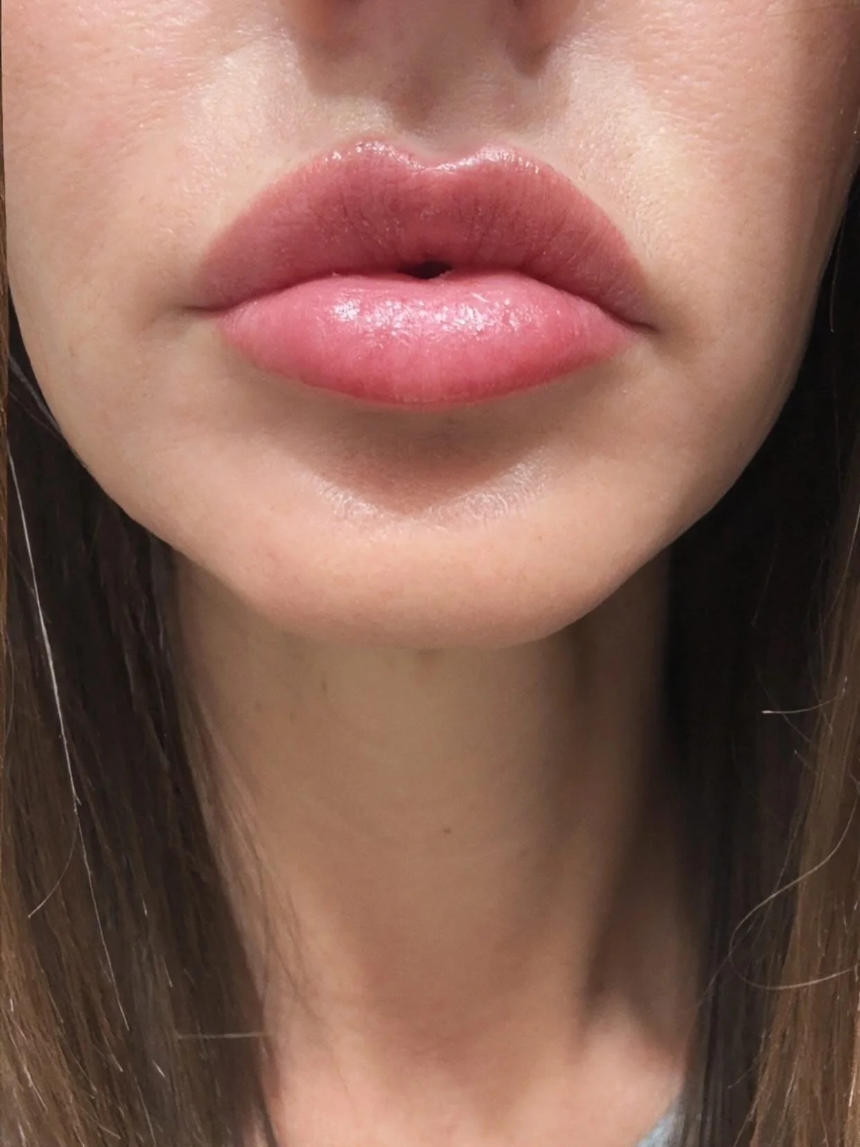 Close-up of a person's lips with glossy pink lipstick, slightly parted.