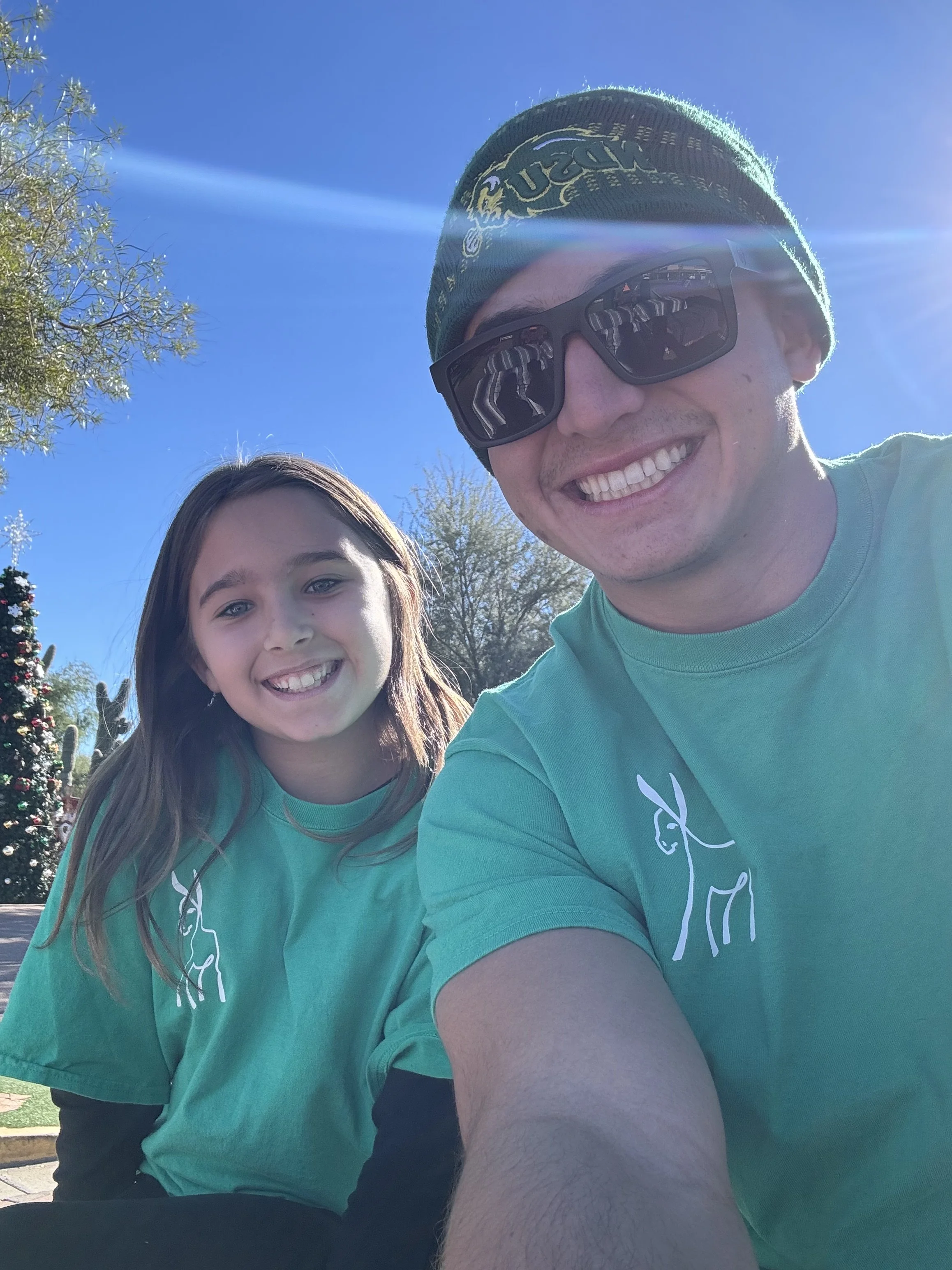 Two youth volunteers smiling close to the camera, with the sun shining behind them