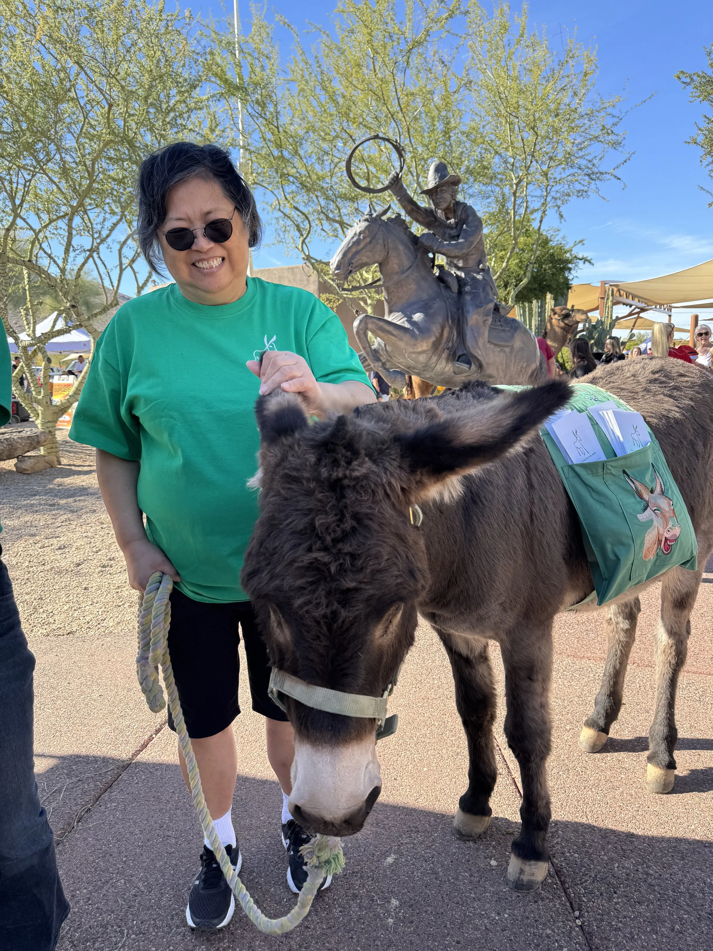 A long-standing volunteer wearing the organization's logo t-shirt, holding a lead line while standing next to a donkey