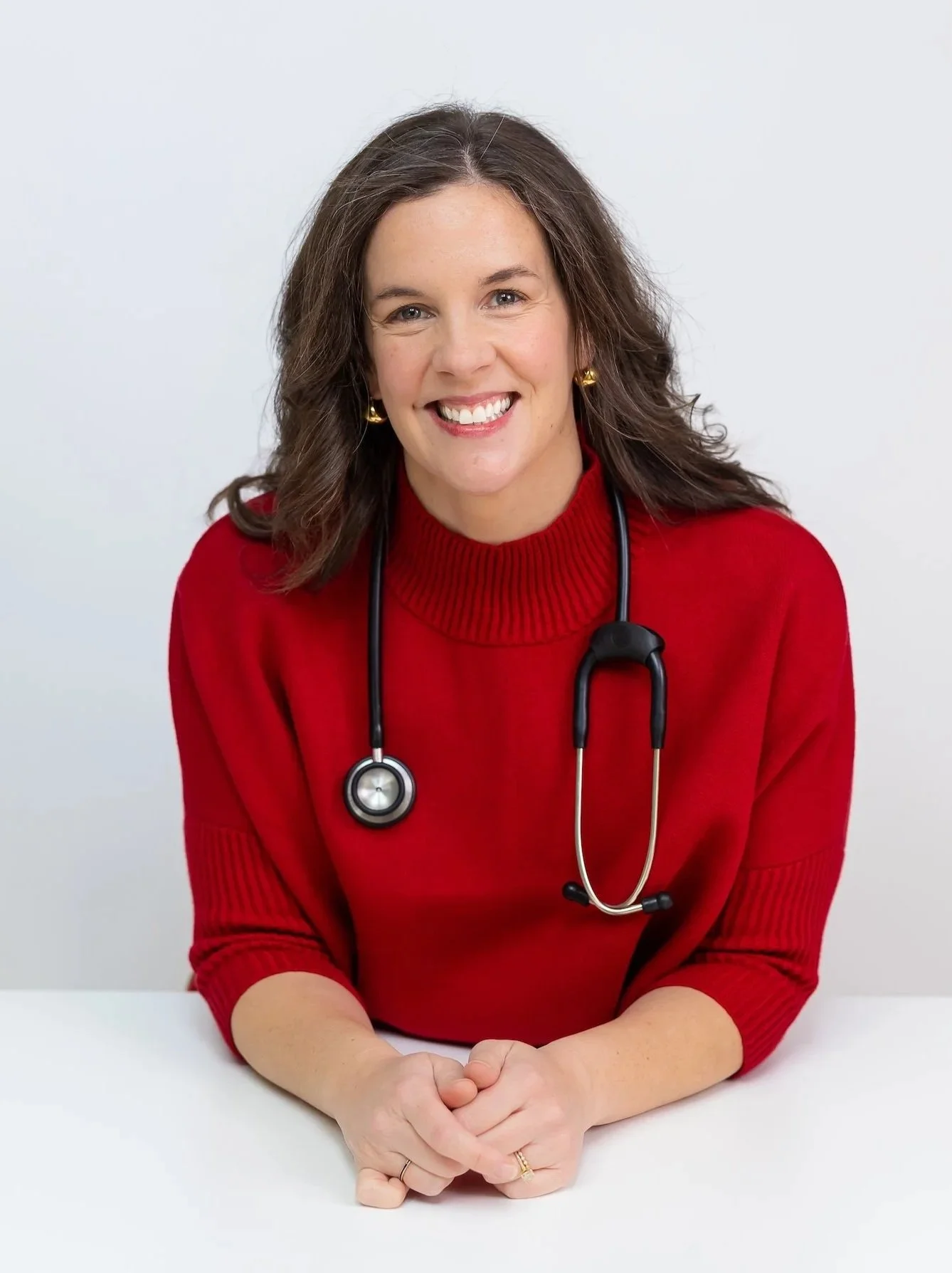 Female healthcare professional wearing a red sweater and stethoscope, smiling at the camera.