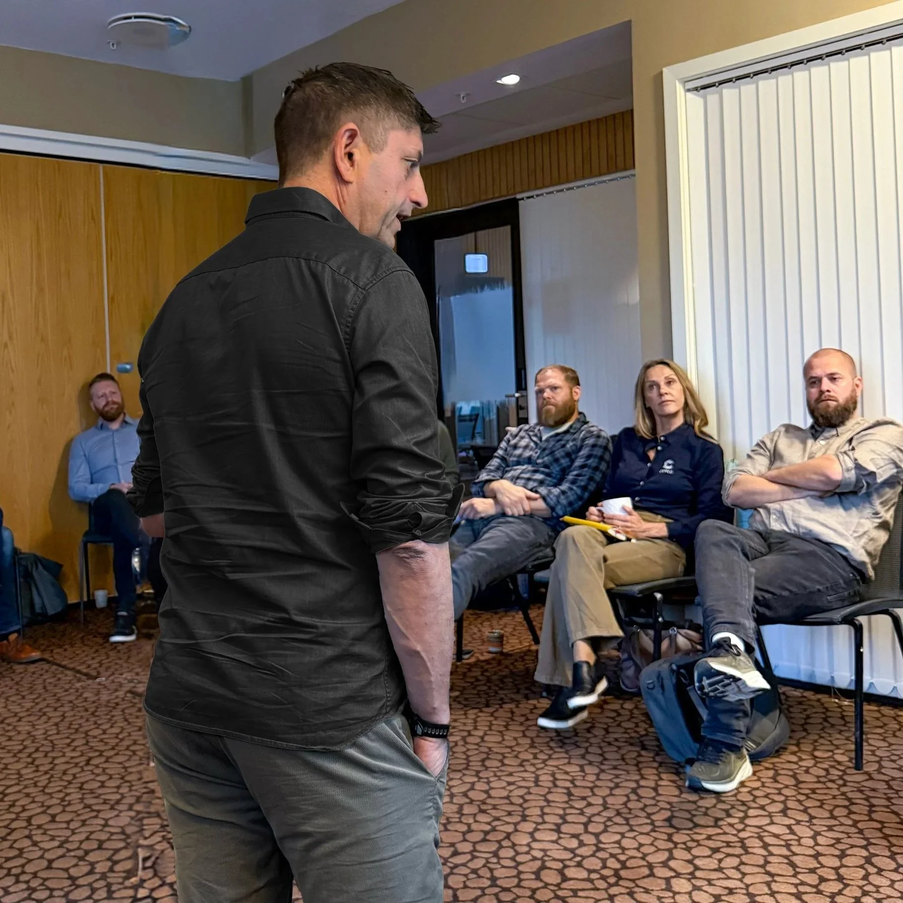 Mann snakker foran en gruppe mennesker i et møterom.