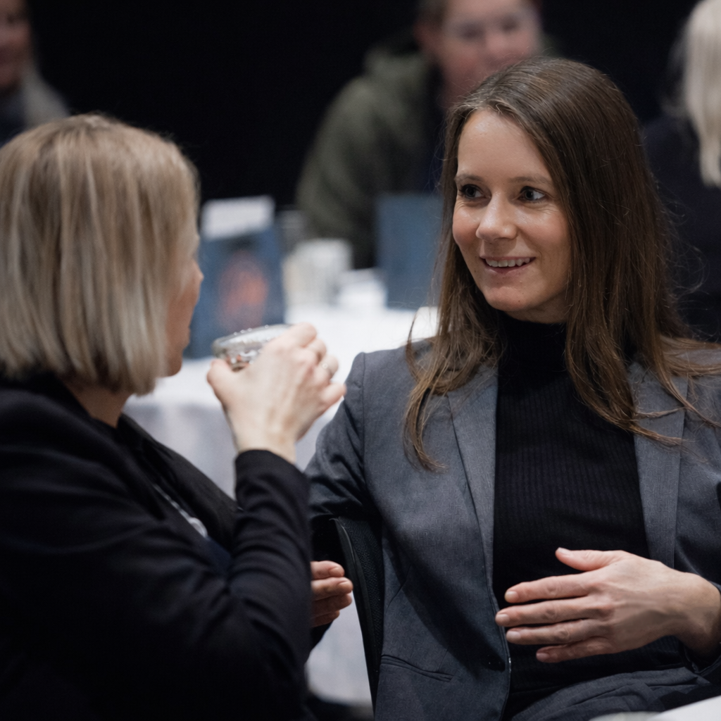 To kvinner snakker og ler mens de spiser og drikker på en formell sammenkomst