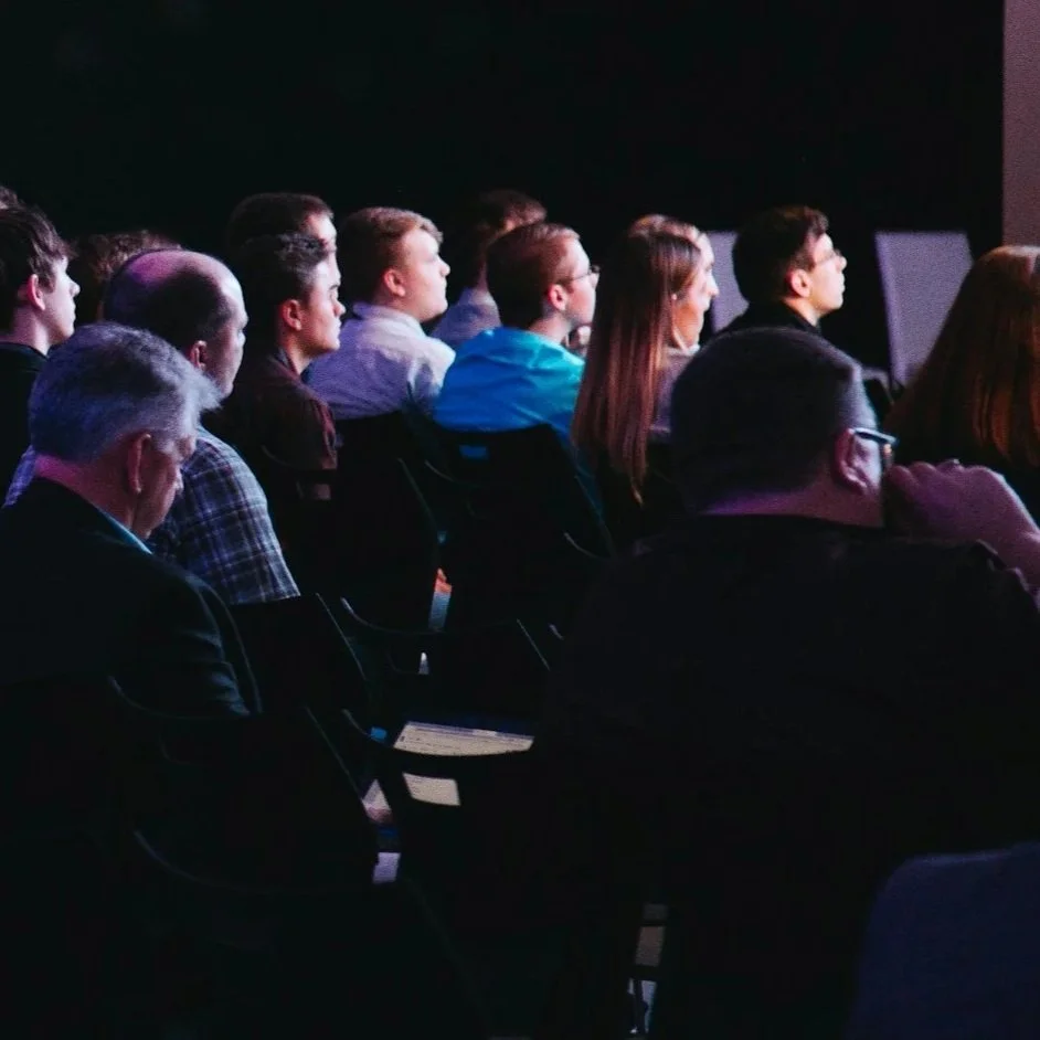 Folk som ser på en skjerm i mørkt rom, reflektert lys fra skjermen.