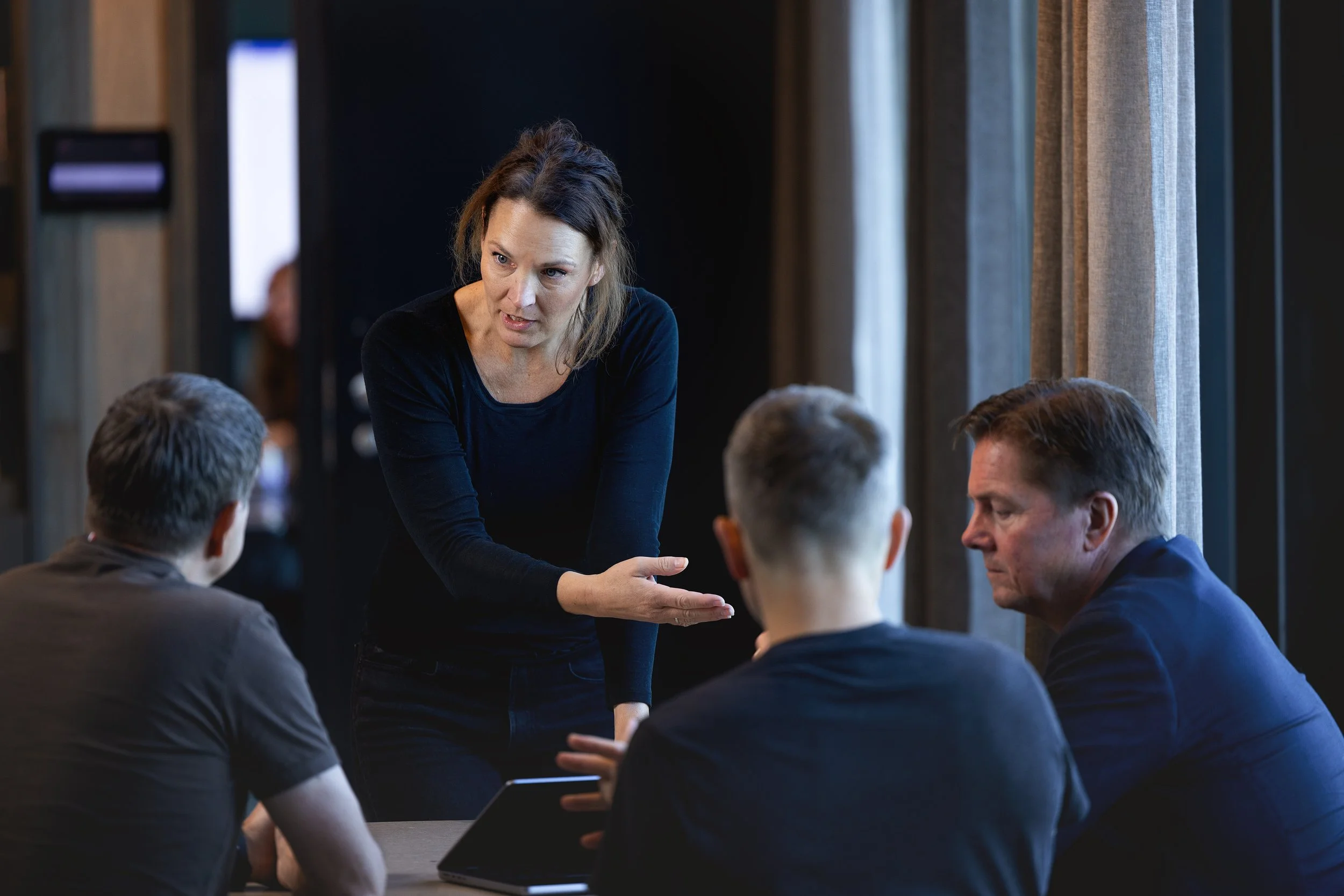 En kvinne snakker med en gruppe menn i et møterom.