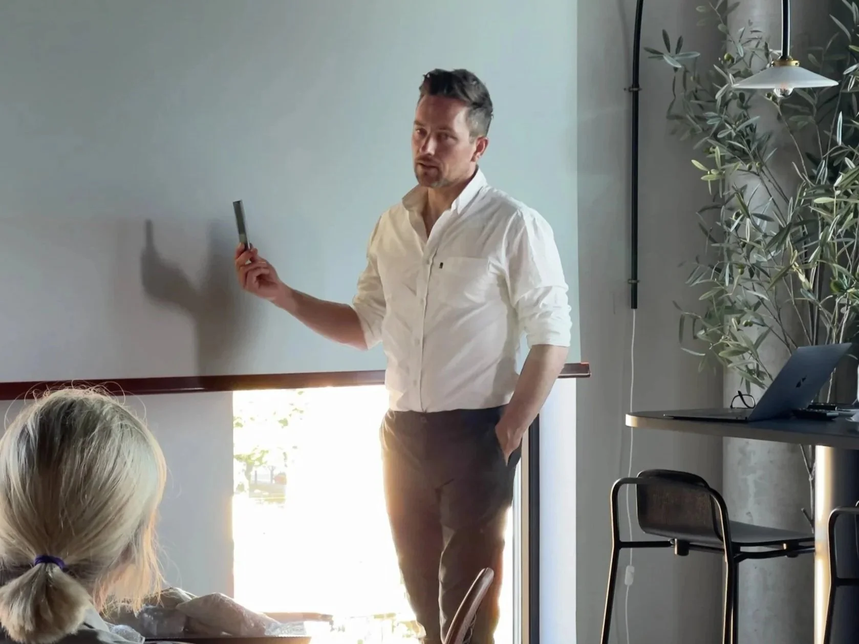 En mann holder en penn foran en gruppe mennesker i et møterom, foran en hvit tavle.