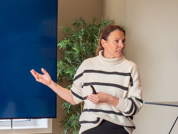 Kvinne holder en pekepenn og snakker foran en skjerm i et møterom.
