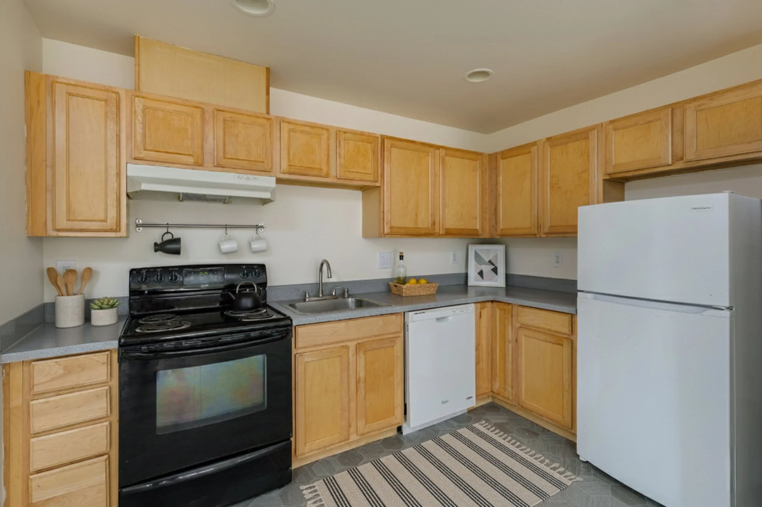 Kitchen with wooden cabinets, black stove, white dishwasher, white refrigerator, gray countertops, and small decorative items.