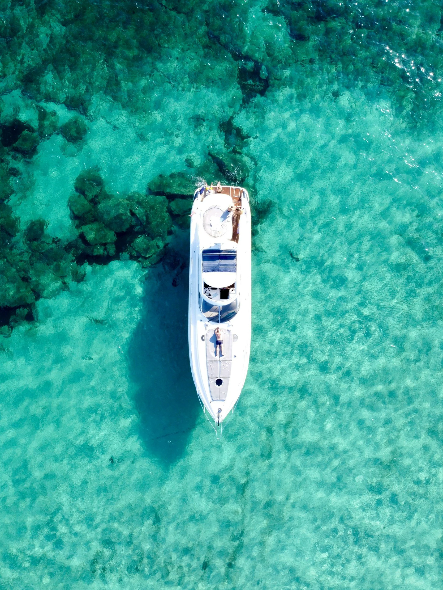 Overhead view of a white yacht floating in clear turquoise water near rocks.