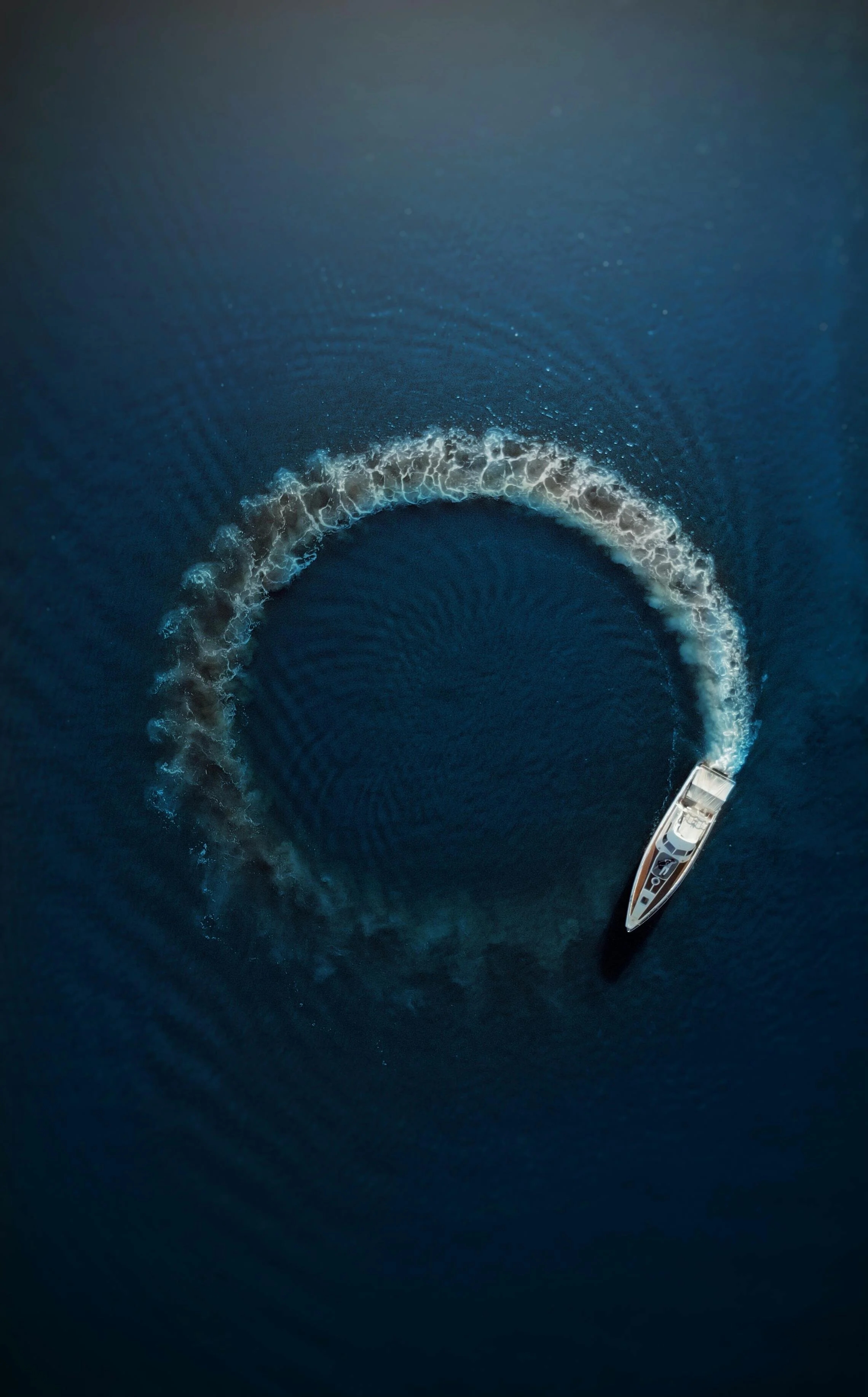 A luxury yacht creating a circular wake on the deep blue water.