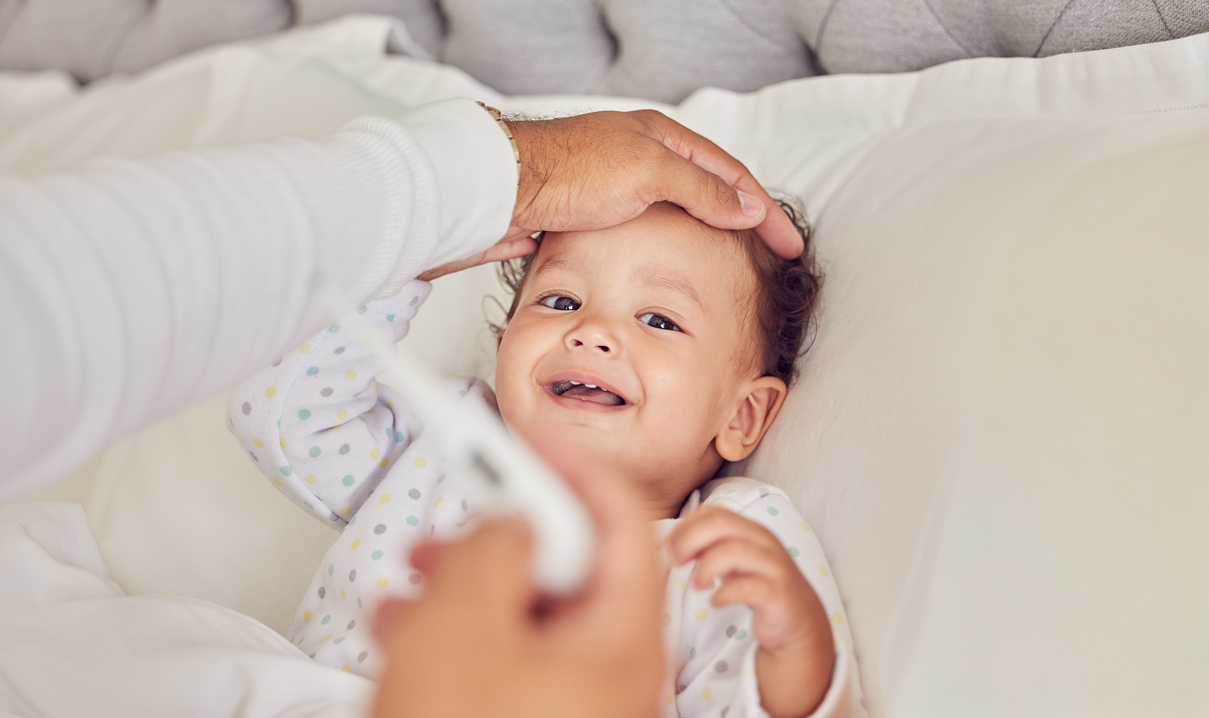 Young child lying in bed, smiling, with a hand on their head, wearing pajamas with colorful polka dots.