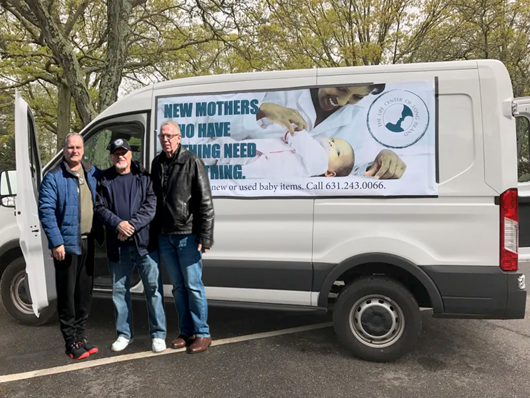 Three men standing in front of a van with a banner about providing baby items. The banner shows an image of a nurse and a baby, with text about helping new mothers in need.