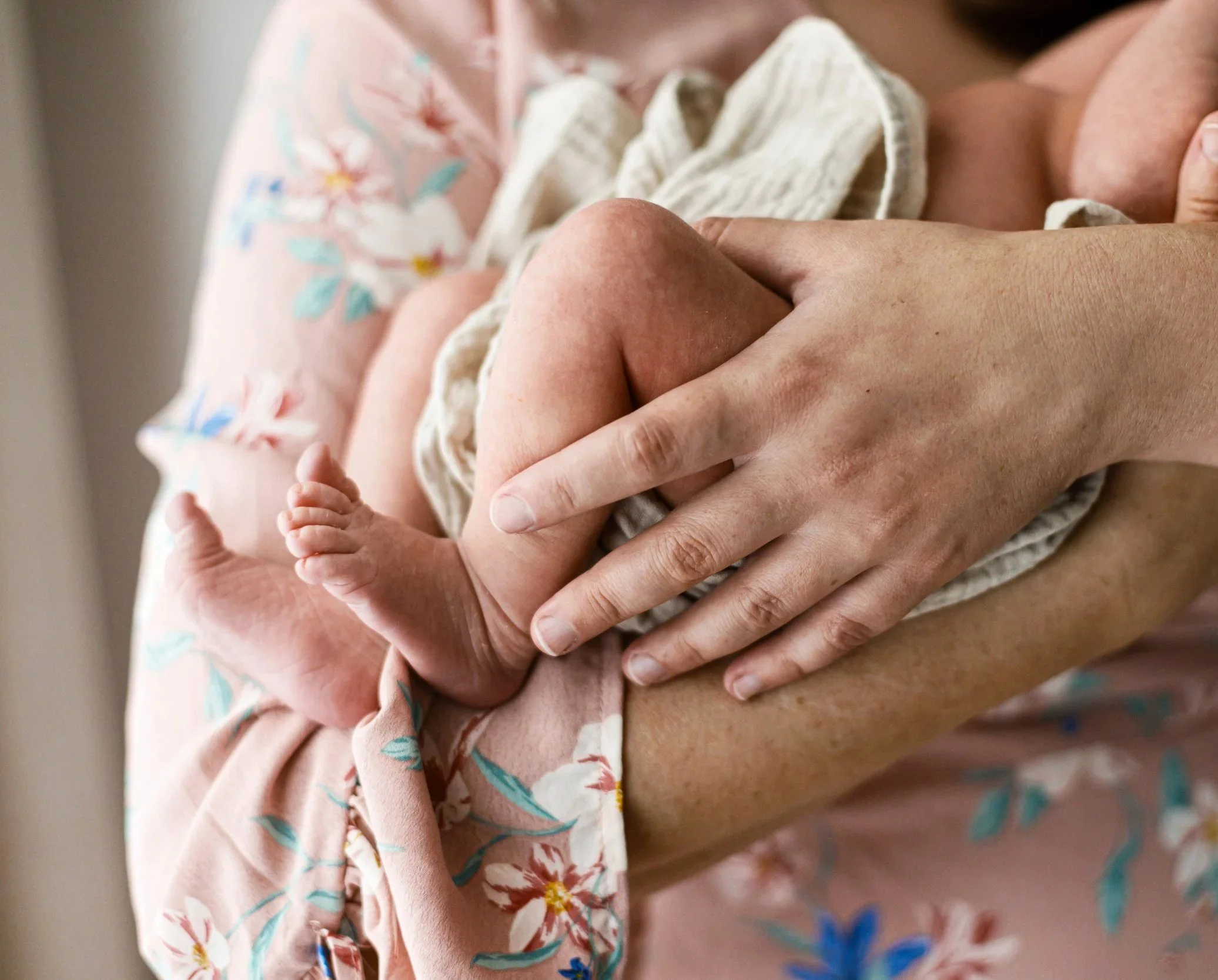 Close-up of a person holding a newborn baby, focusing on the baby's tiny hand resting on the adult's hand.