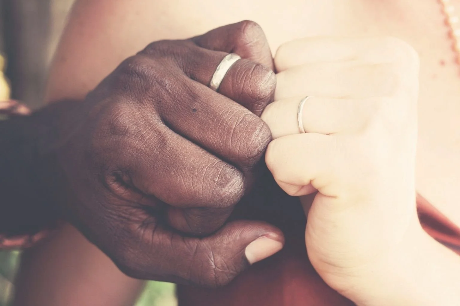 Close-up of two hands, one dark-skinned and the other light-skinned, holding each other's fingers in a gesture of unity.
