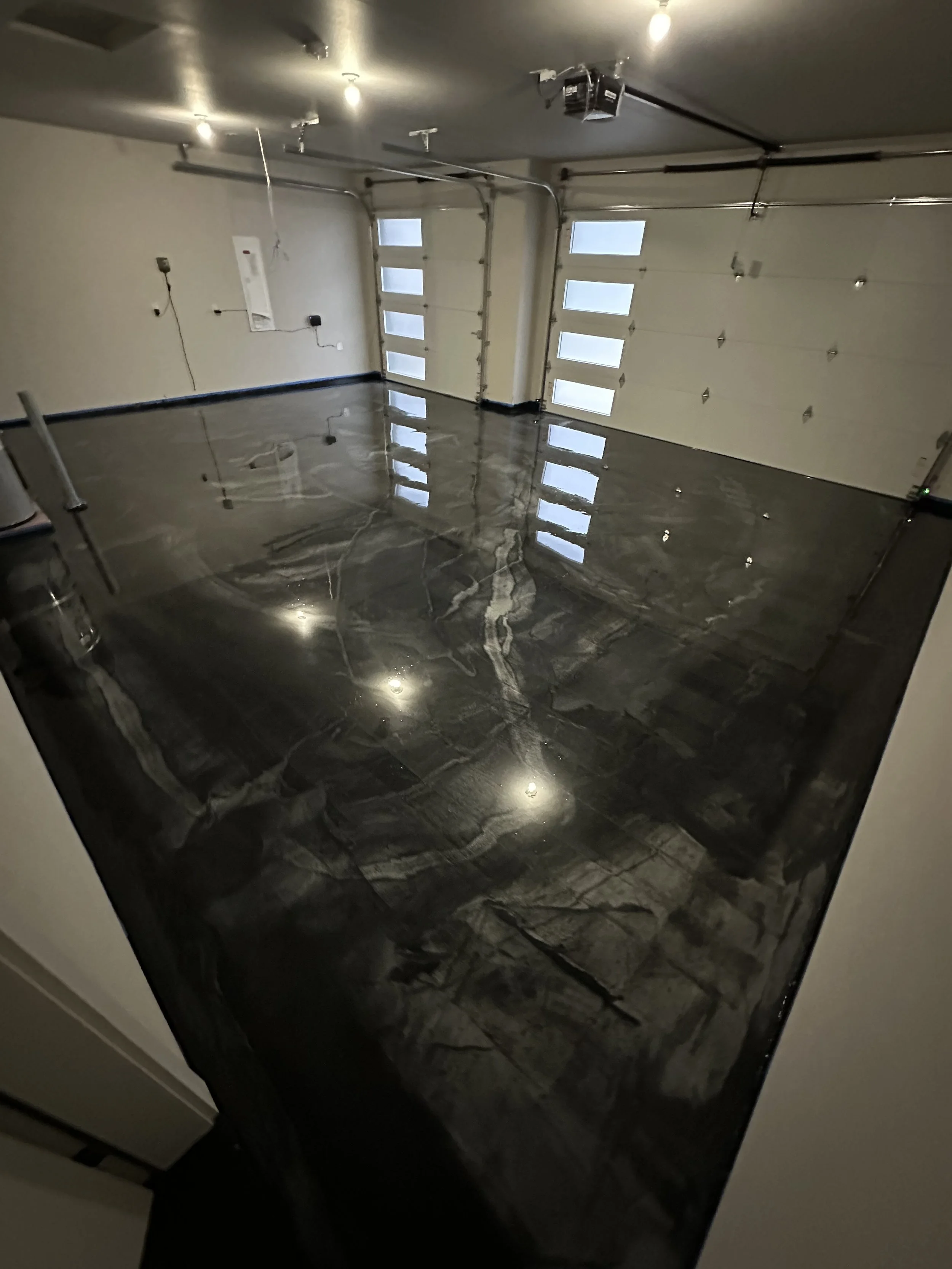 Empty garage with a polished black marble floor, white walls, and two white garage doors with windows.