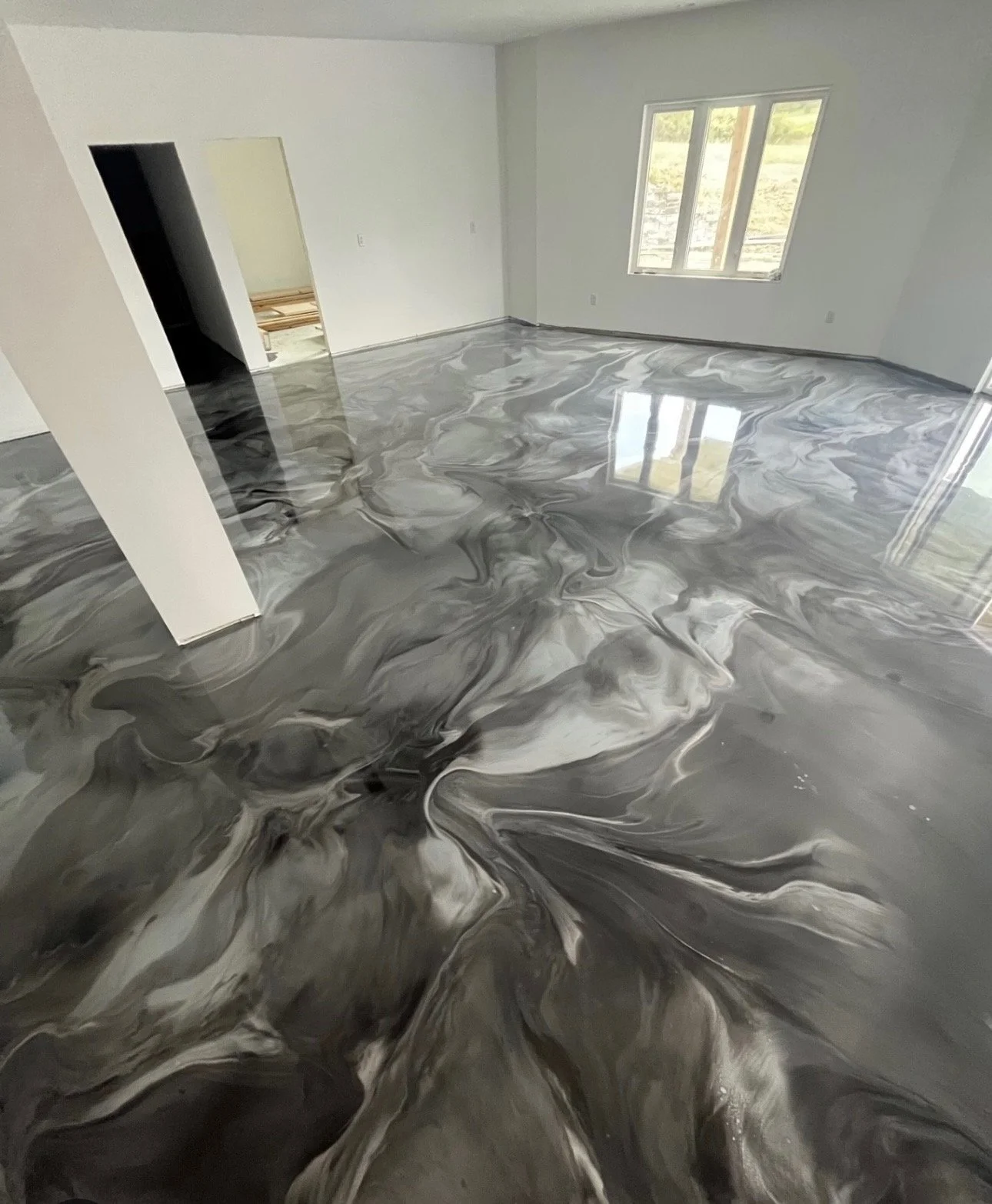 Room with marble-style black, white, and gray epoxy floor, white walls, large window, and doorway to another room.