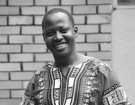 Smiling man wearing a patterned dashiki standing in front of a brick wall.