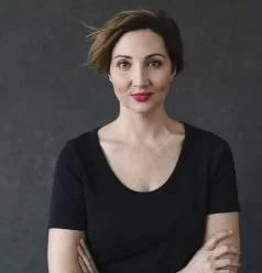 Portrait of a woman with short, styled hair, wearing a black top, against a dark background.