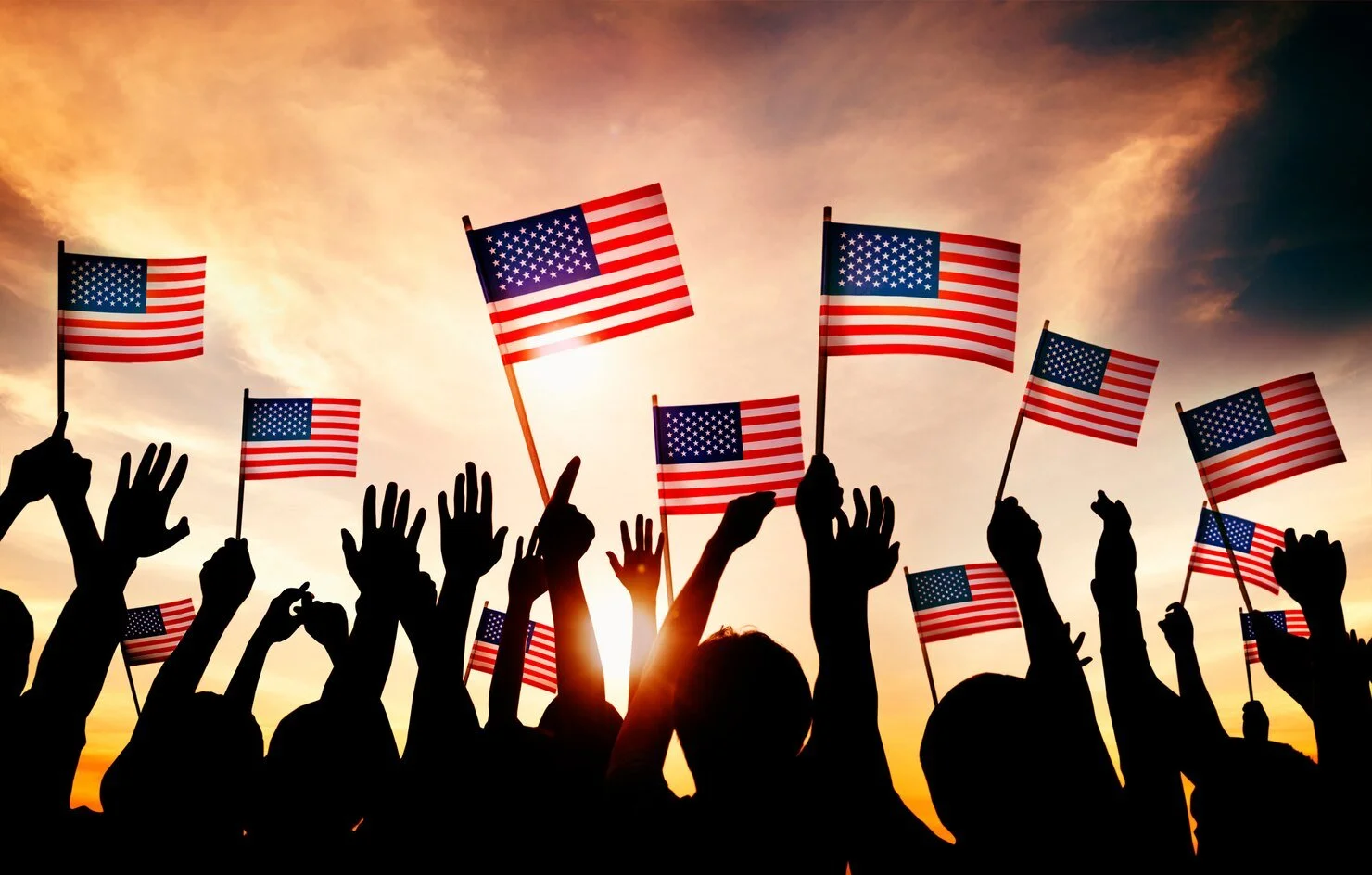 Silhouettes of people holding American flags during sunset.