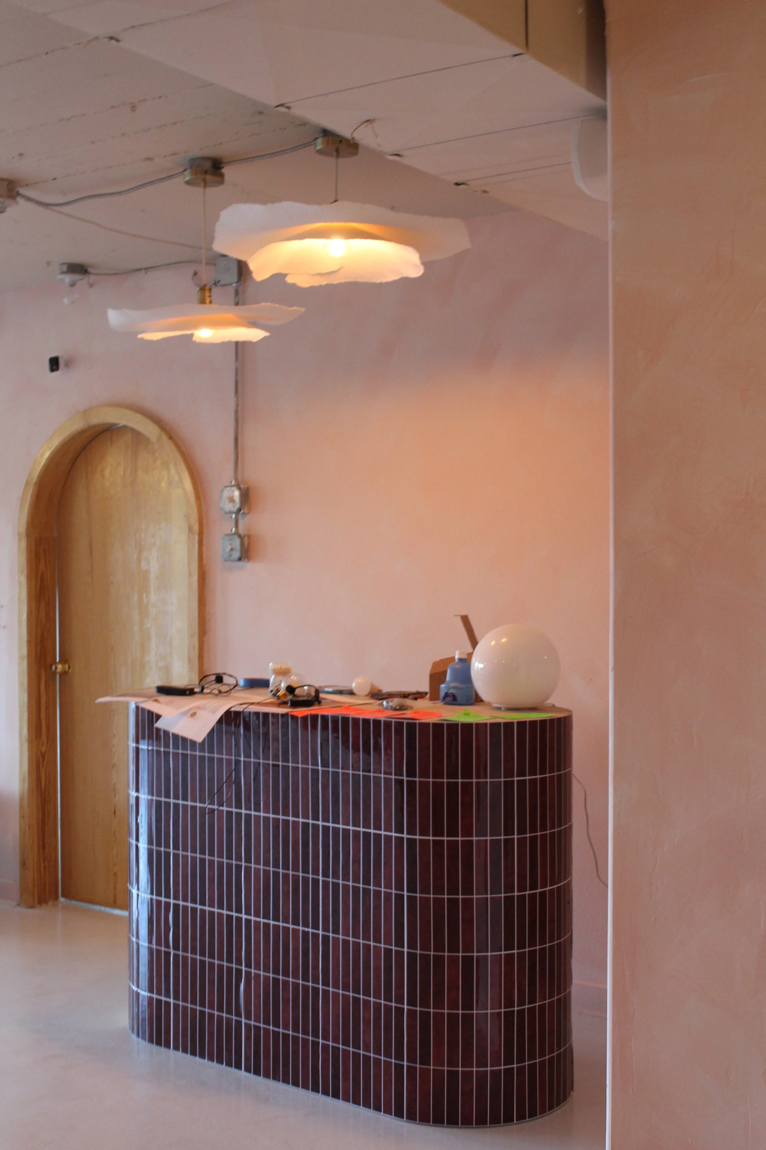 Warm reception area at Third Space Studios featuring a curved dark-tiled desk, arched doorway, and cloud pendant lighting