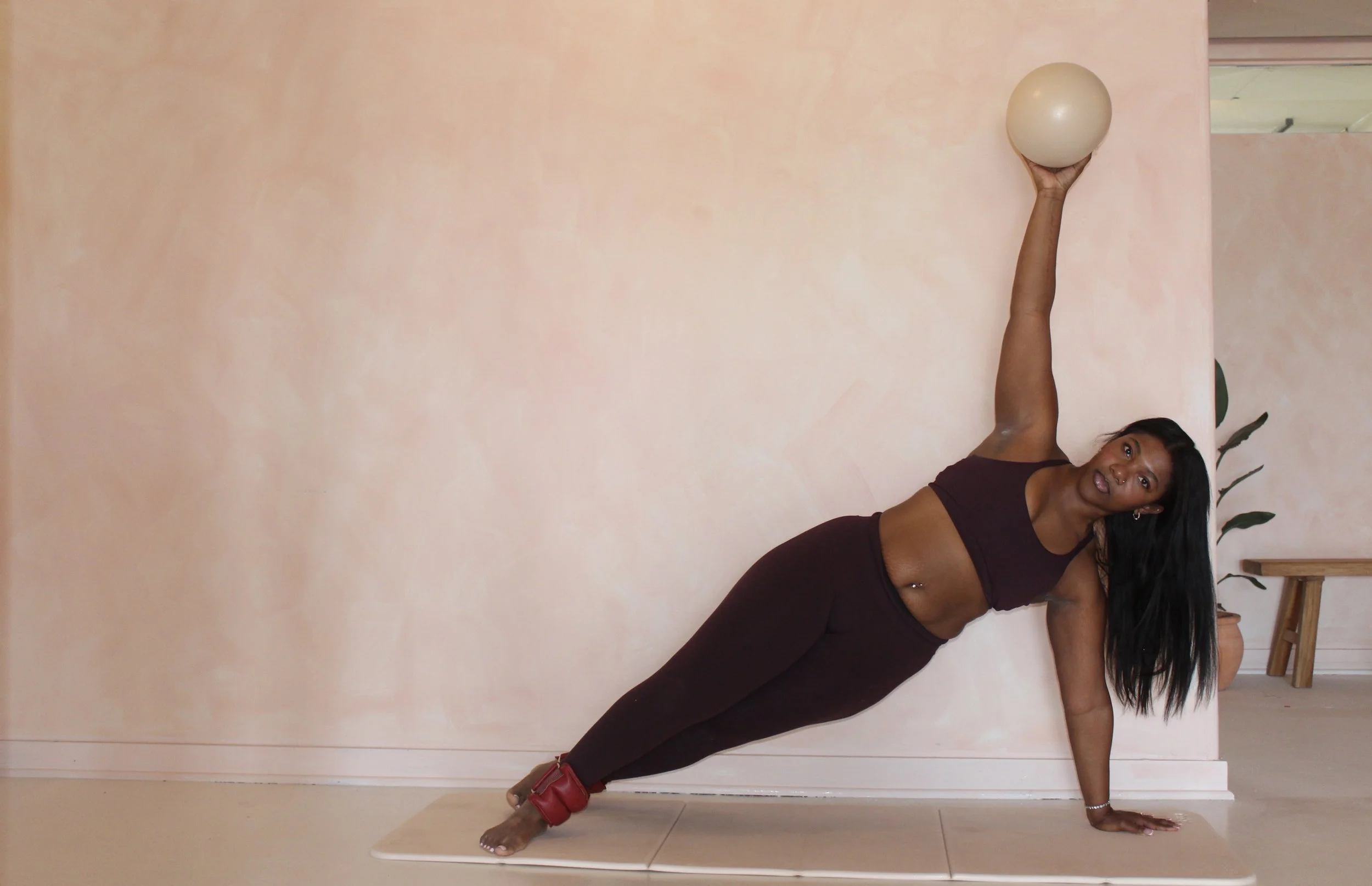 Pilates instructor demonstrating a side plank with a small ball at Third Space Studios in Houston, TX