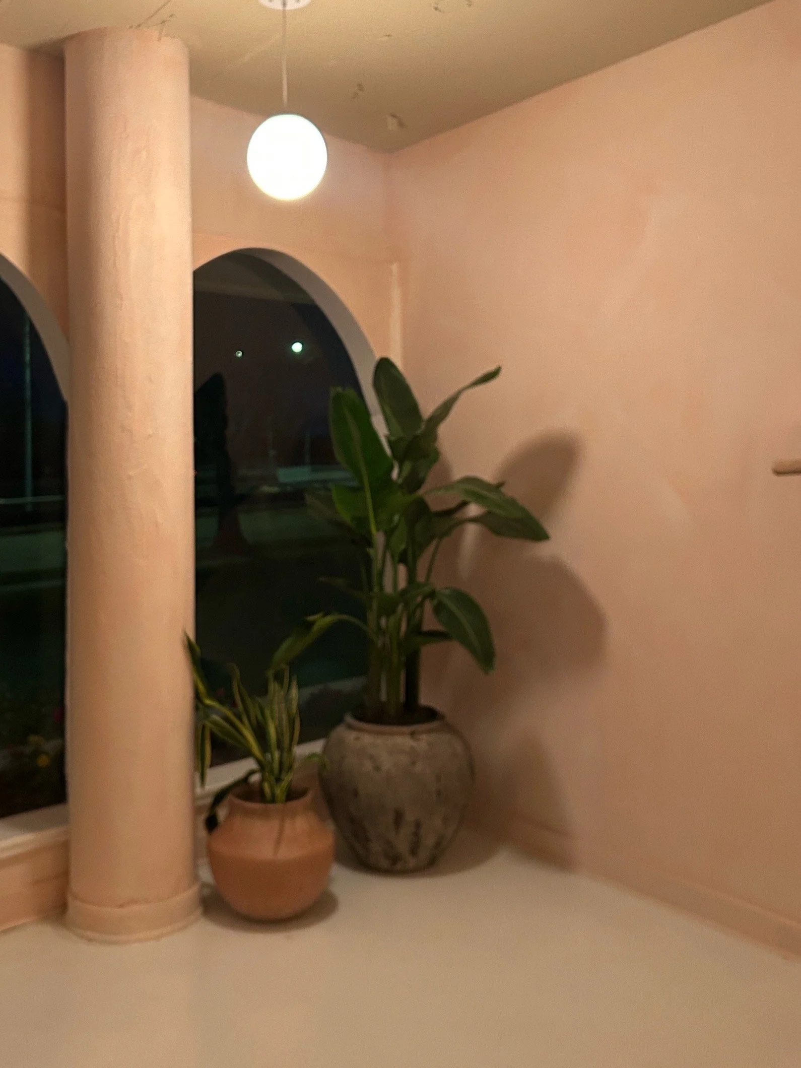 Warm-toned studio entryway with arched doorways, blush walls, a globe pendant light, and tropical plants at Third Space Studios in Houston.