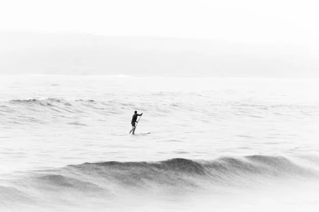 A person stand-up paddleboarding on the ocean with small waves, in black and white.