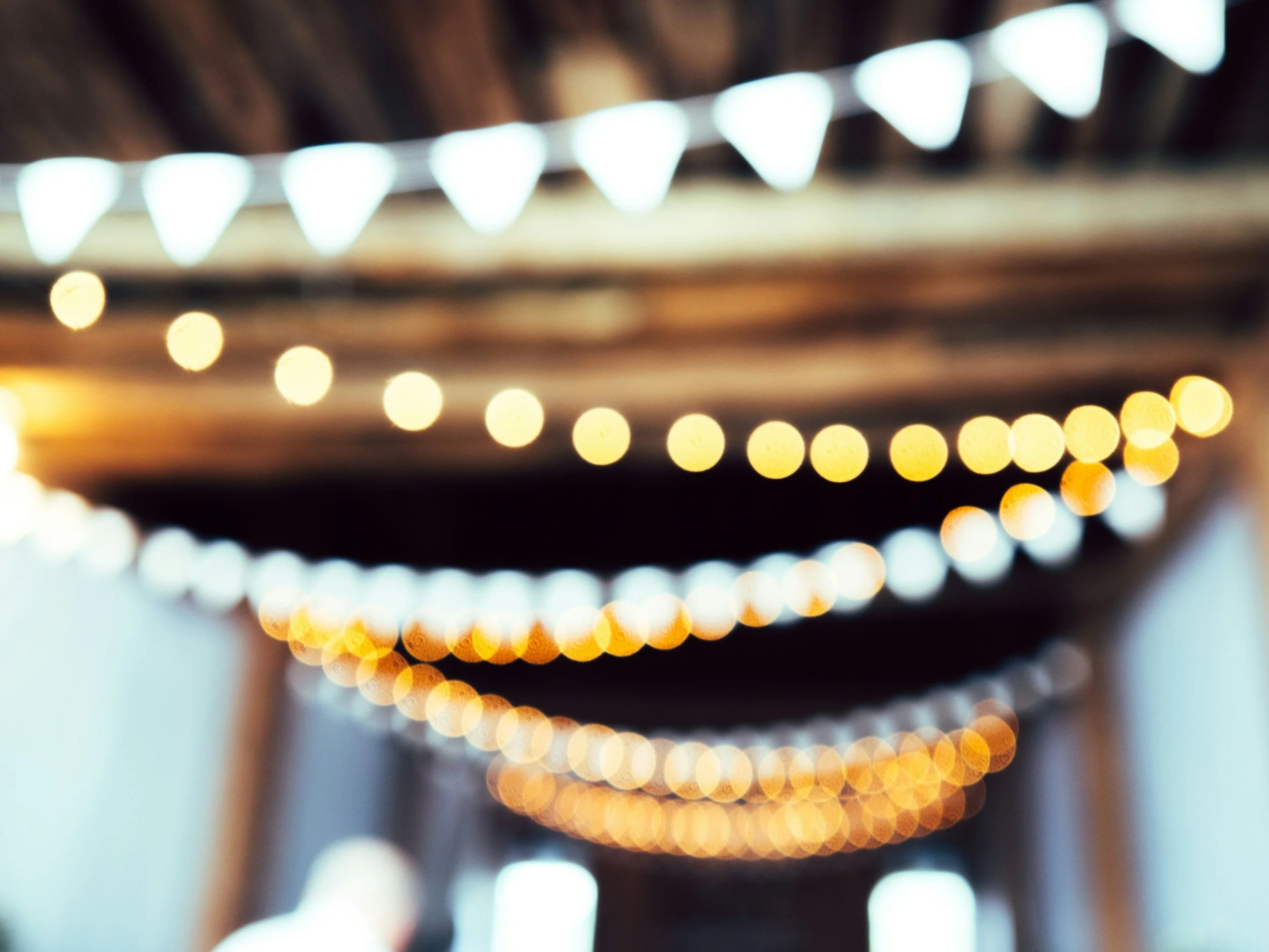 Outdoor covered area with string lights hanging from wooden beams, blurred background.