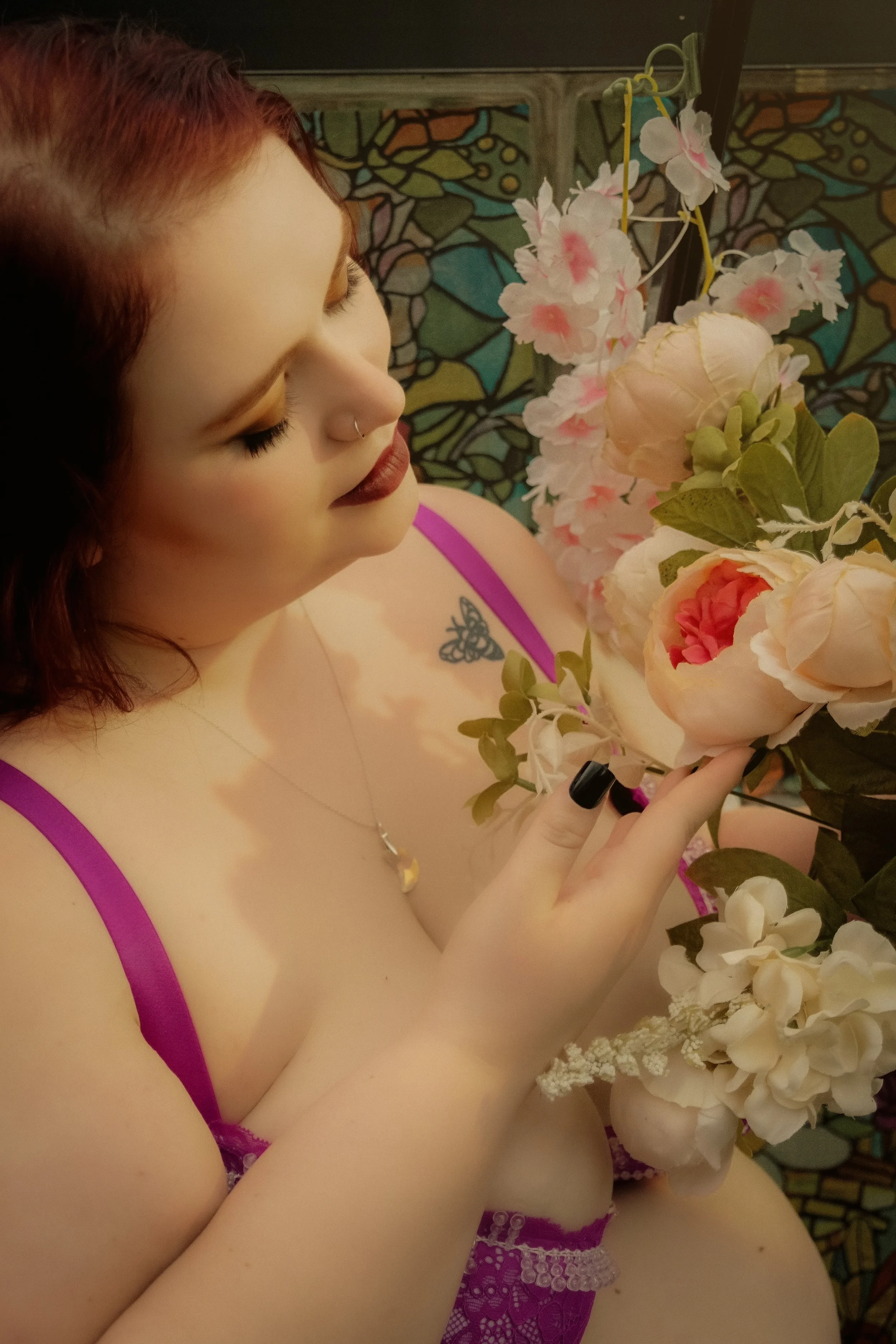 A woman with red hair and a nose piercing is holding a bouquet of pink and white flowers.
