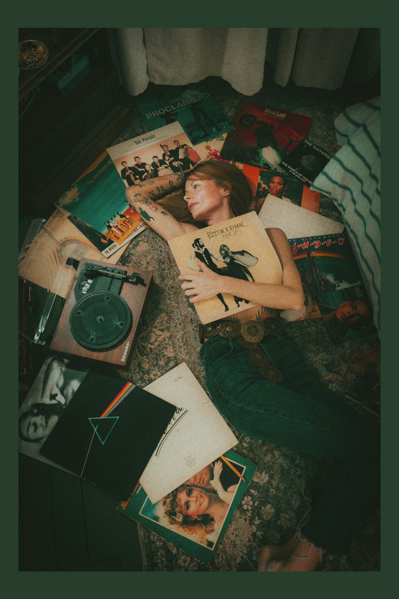 A woman lying on the floor surrounded by vinyl records and a turntable, holding a Fleetwood Mac album cover, with vintage-inspired, muted tones and a casual setting.
