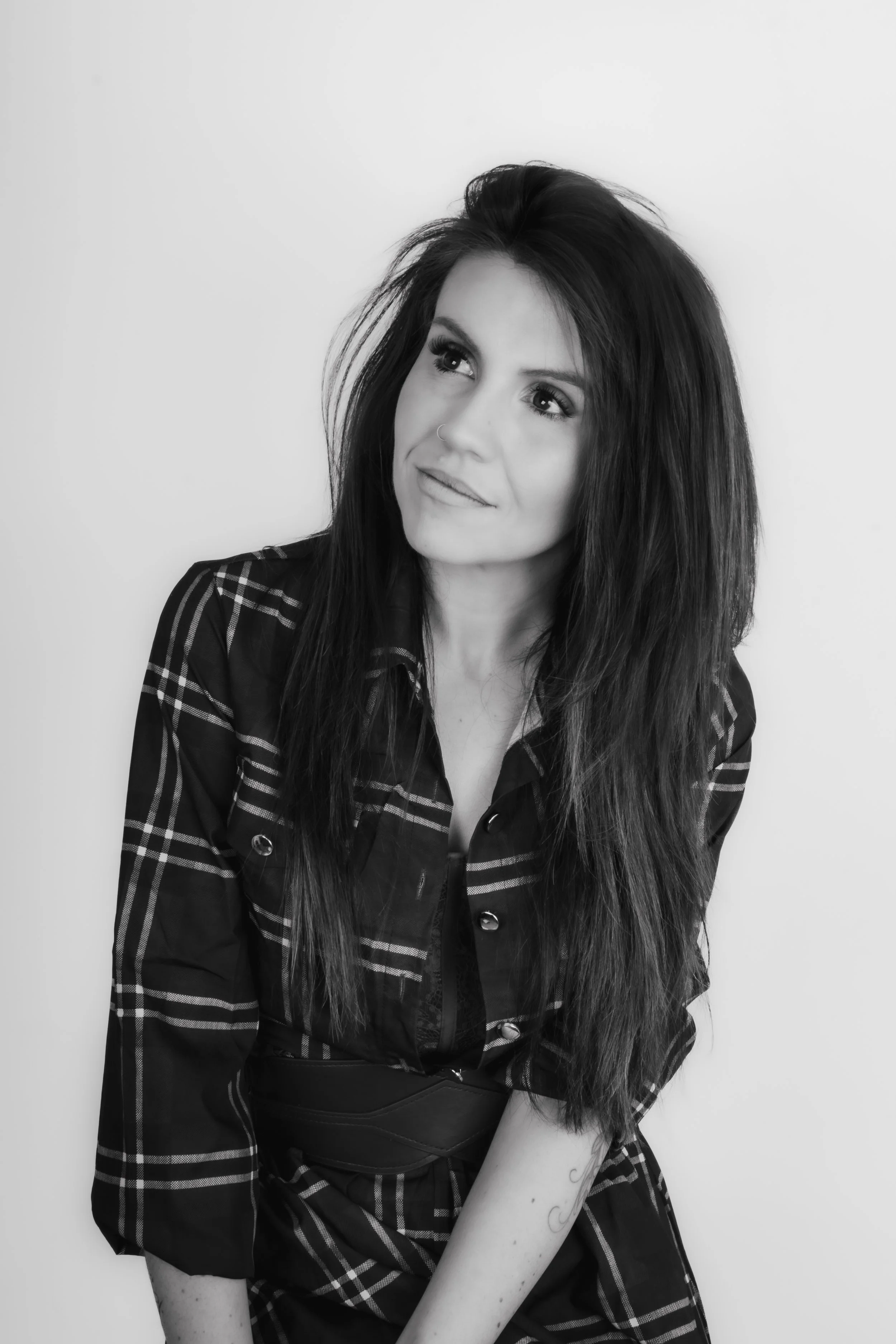 Black and white photo of a woman with long, dark hair wearing a plaid shirt, looking to her right with a slight smile.