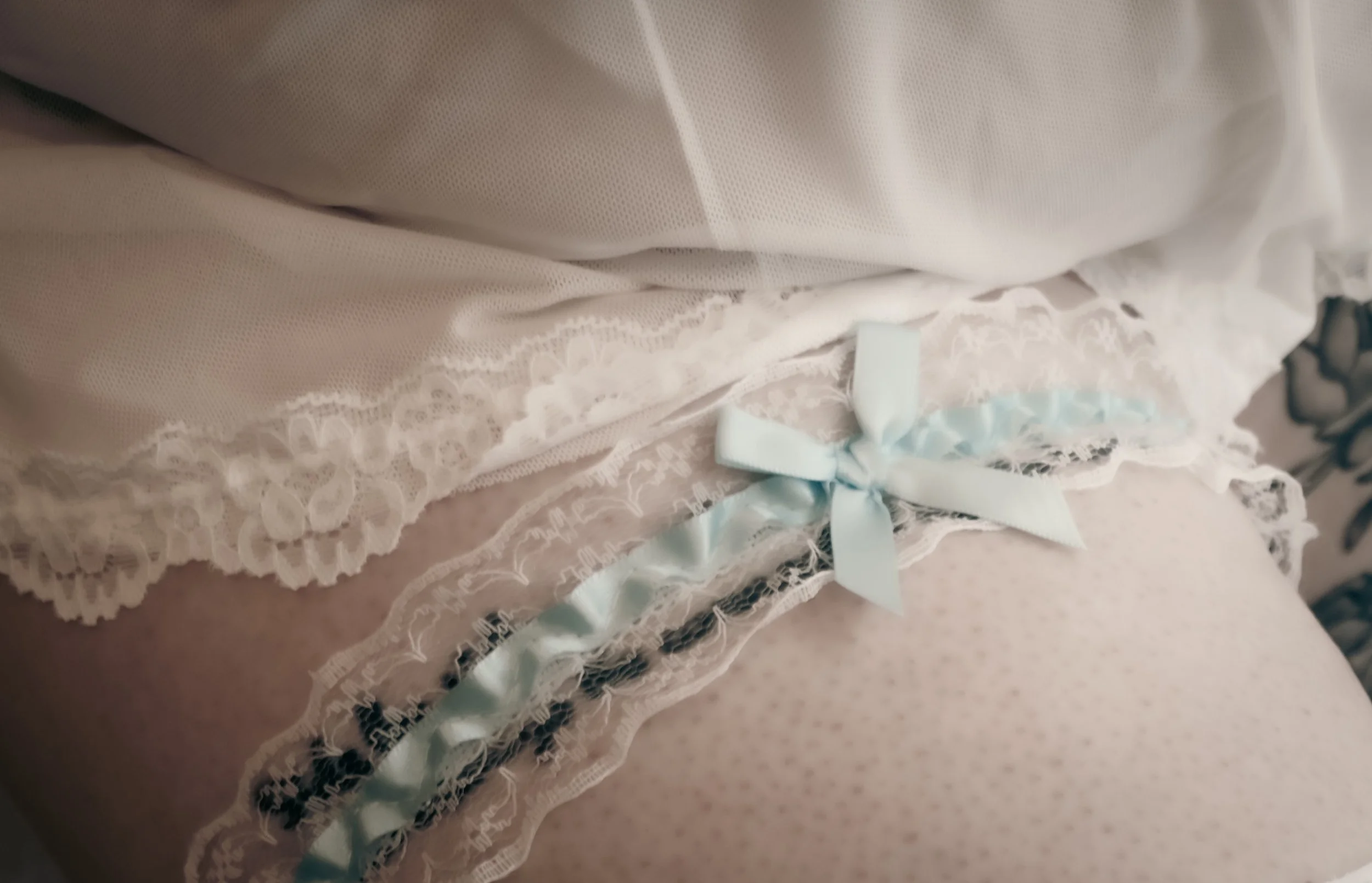 Close-up of a bed with white and pastel-colored lace-trimmed bedding and a satin bow at the edge.
