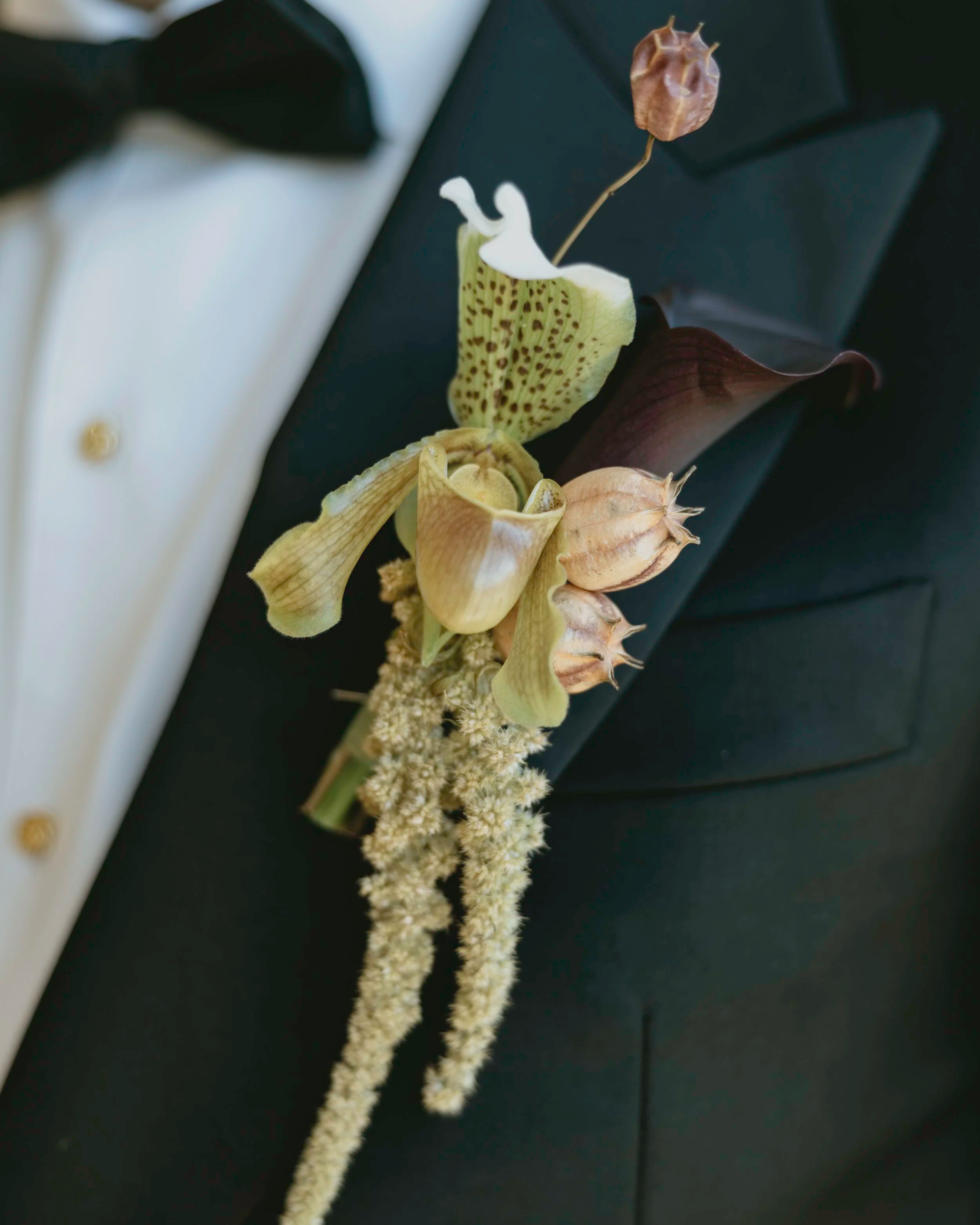 Close-up of boutonnière with calla lily flowers and leaves, worn with formal attire. marigolds florals.