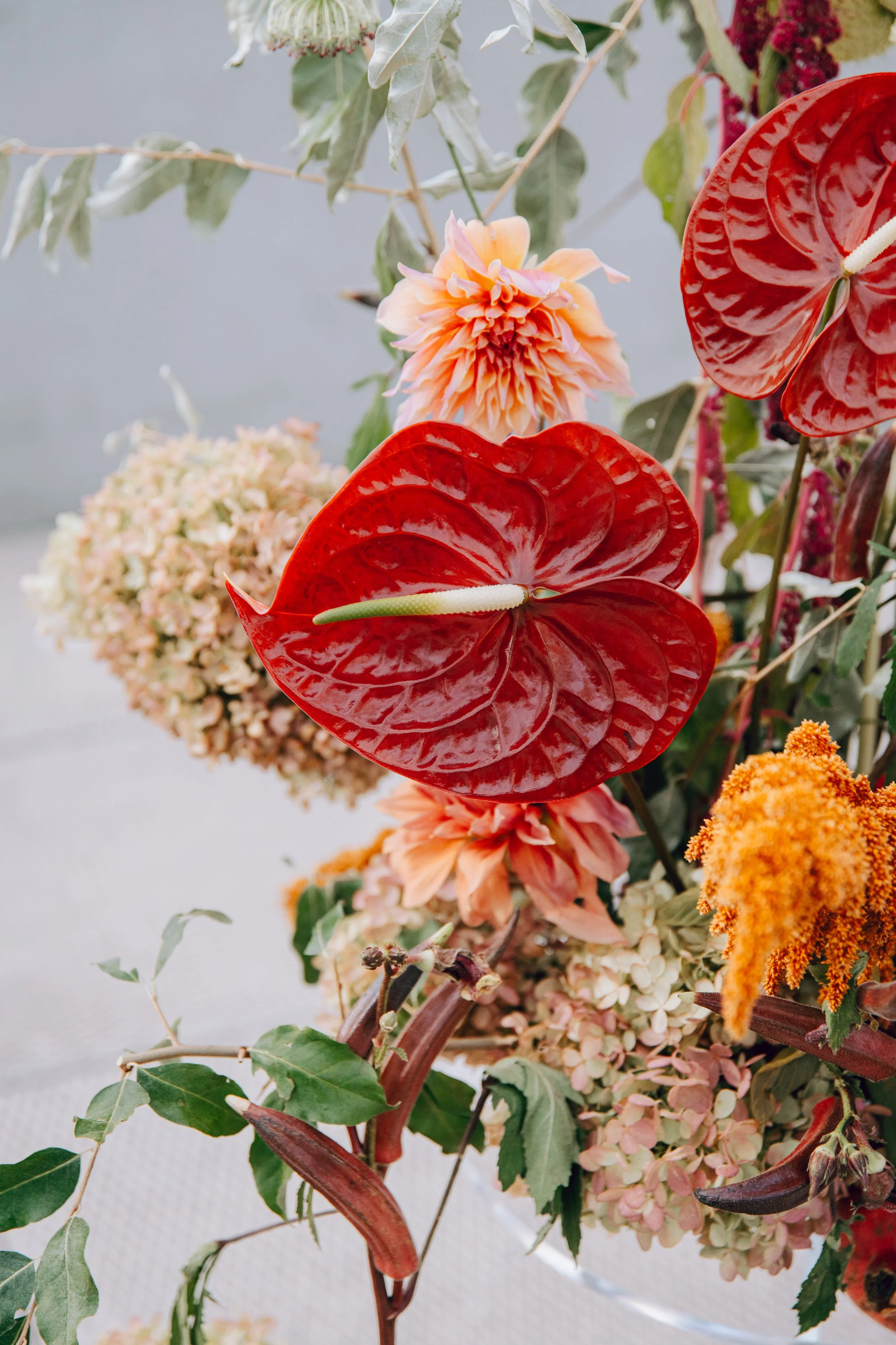 A colorful arrangement of flowers including red anthuriums, peach dahlias, cream hydrangeas, and green foliage. marigolds florals nyc florist wedding florals the w loft wedding pedestal wedding ceremony anthurium 