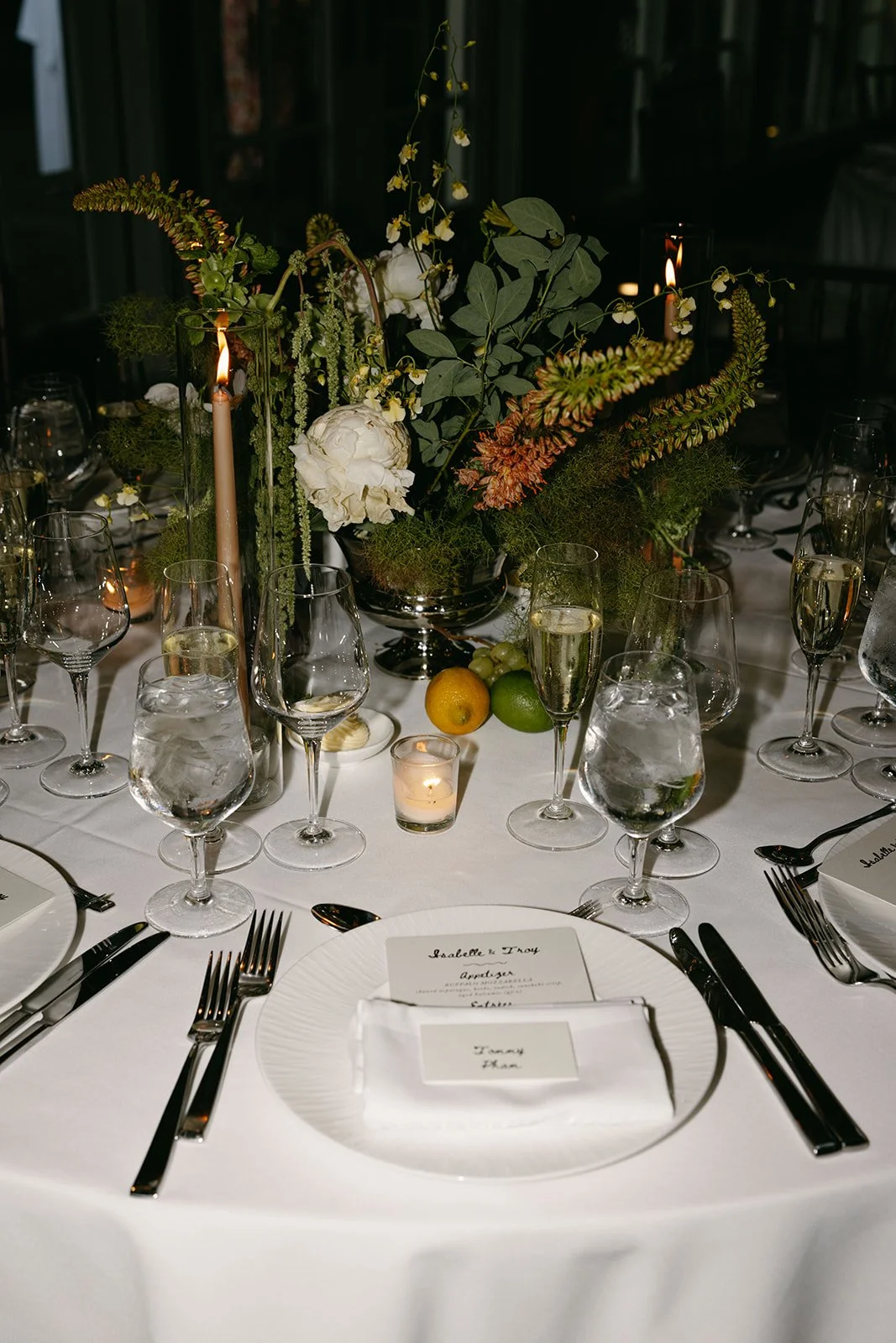 Elegant dinner table with white tablecloth, floral centerpiece, candles, and place settings with glasses, plates, and utensils. marigolds florals nyc florist wedding florals central park boathouse wedding