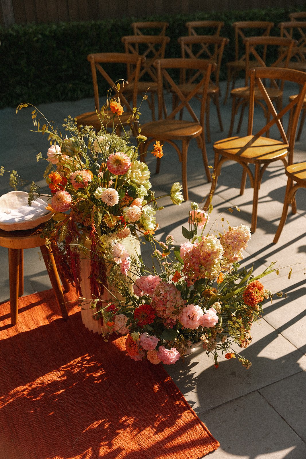Colorful floral arrangement with pink, orange, and white flowers on a table outdoors, with wooden chairs in the background. marigolds florals